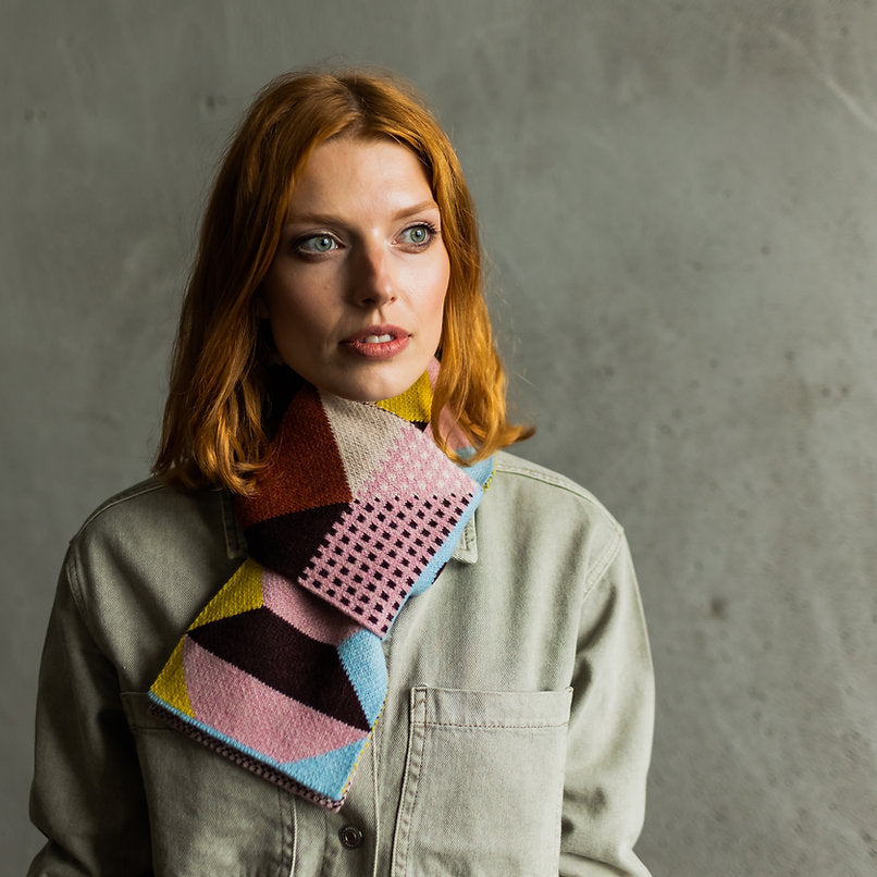Geometric patterned knit scarf in pink, brown, blue, and yellow.