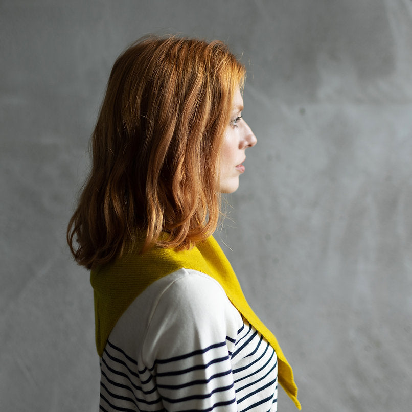 Woman with shoulder-length auburn hair wearing a mustard yellow cowl neck sweater over a navy and white striped shirt.