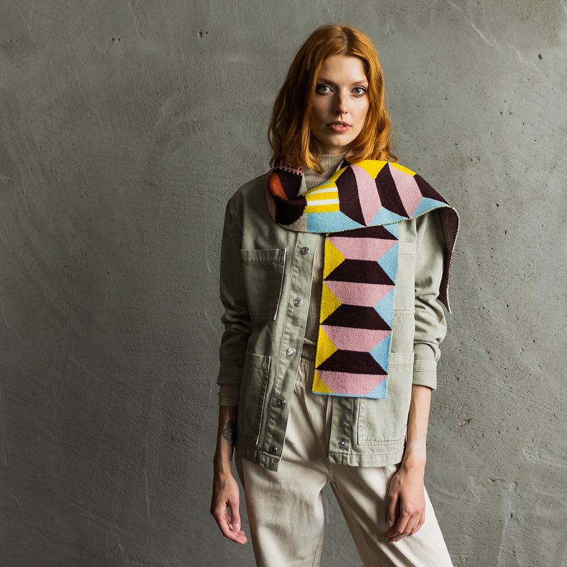 Geometric patterned scarf in pink, brown, yellow, and blue; worn by a model over a sage green utility jacket.