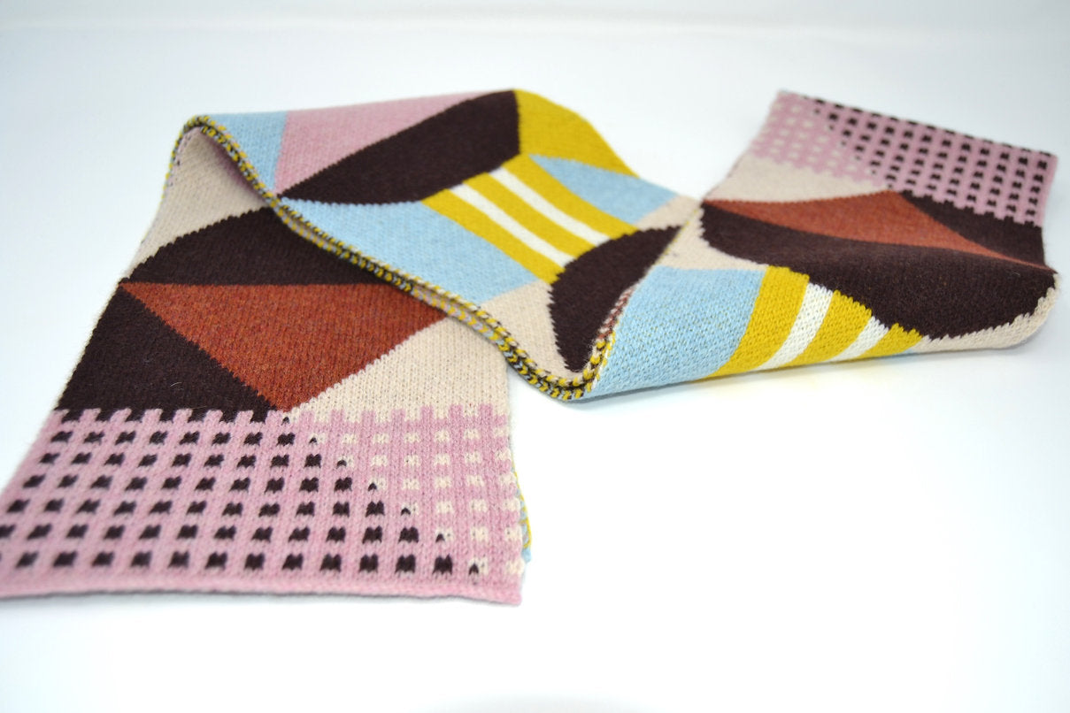 Geometric patterned knit scarf in brown, pink, beige, light blue, and mustard yellow.