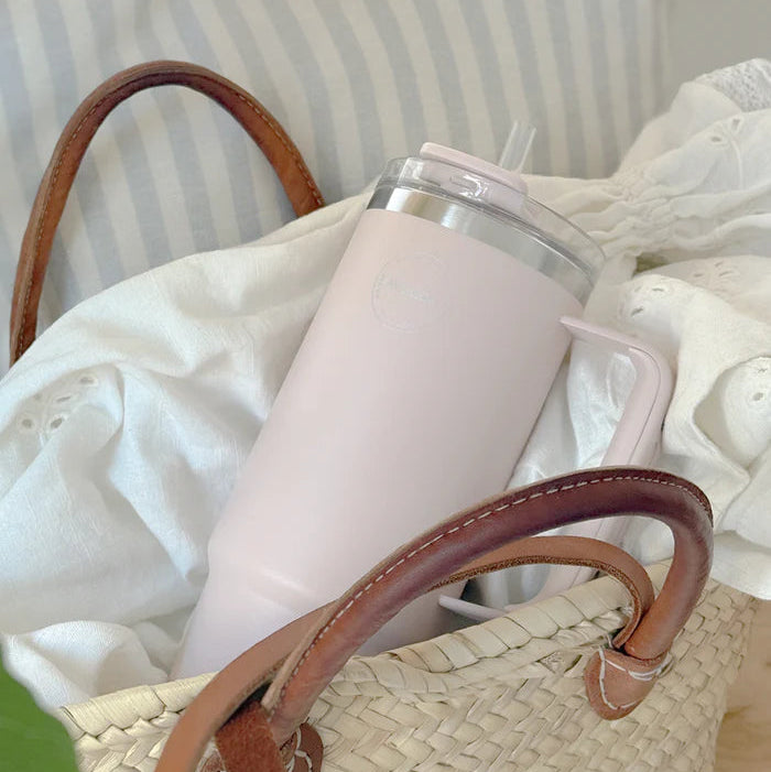 Pink mug with a straw in a woven basket on a light background