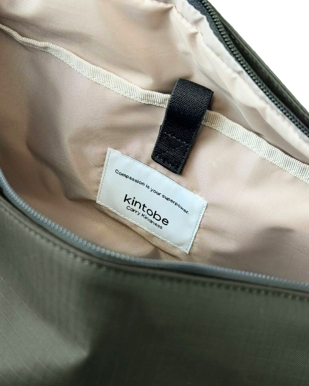 Olive green Kintobe bag interior showing a beige lining, zipper, and small black strap.