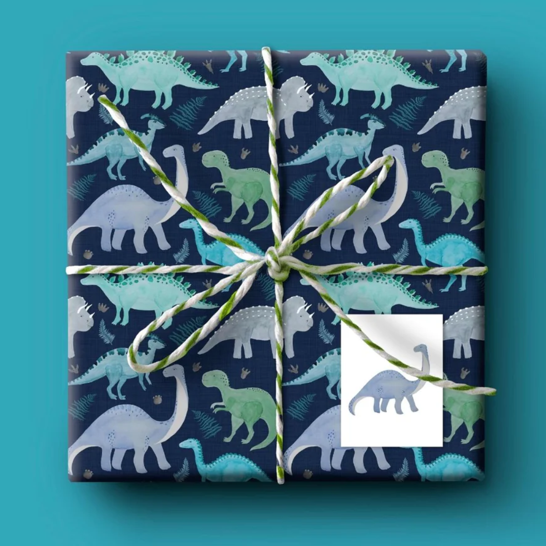 Gift wrap featuring a repeating pattern of watercolor dinosaurs in teal and blue on a dark navy background.
