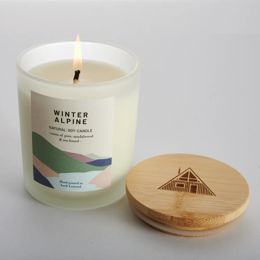 Lit Winter Alpine natural soy candle in frosted glass jar with a bamboo lid; pine, sandalwood, and sea fennel scent.