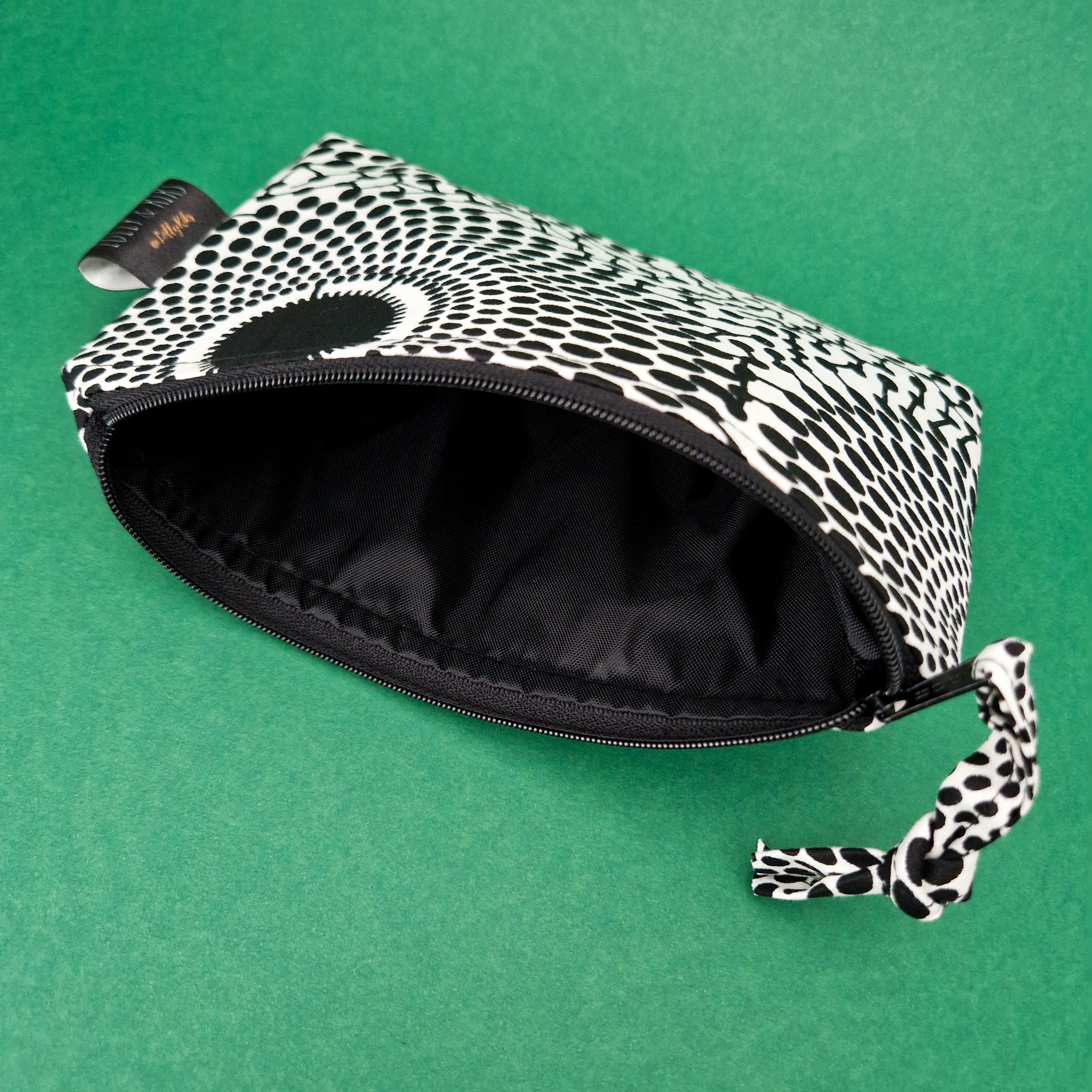 Black and white patterned zippered pouch open to reveal a black interior.  The fabric features a repeating dot design.