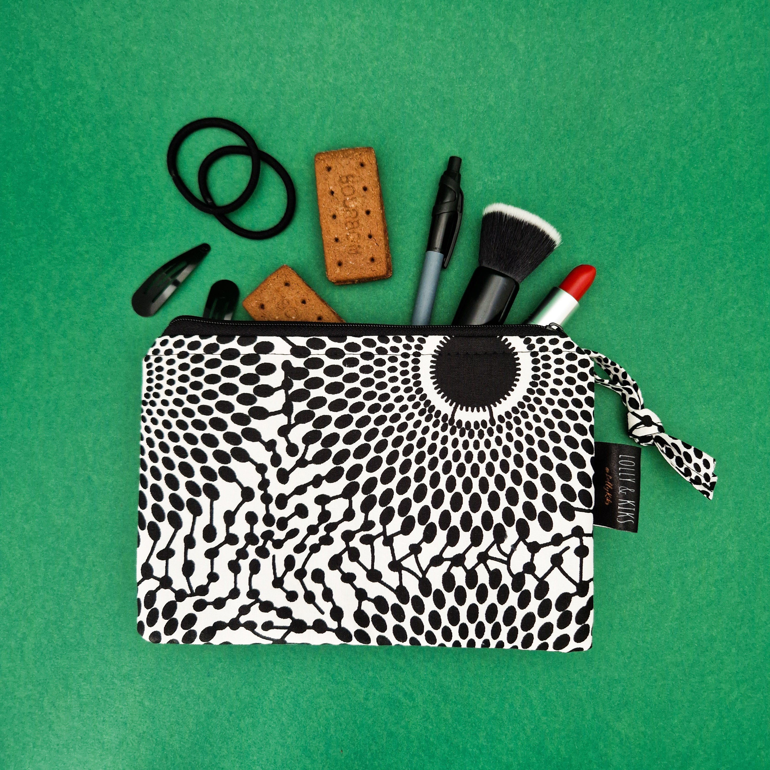 Black and white patterned cosmetic bag filled with makeup, hair accessories, and biscuits.