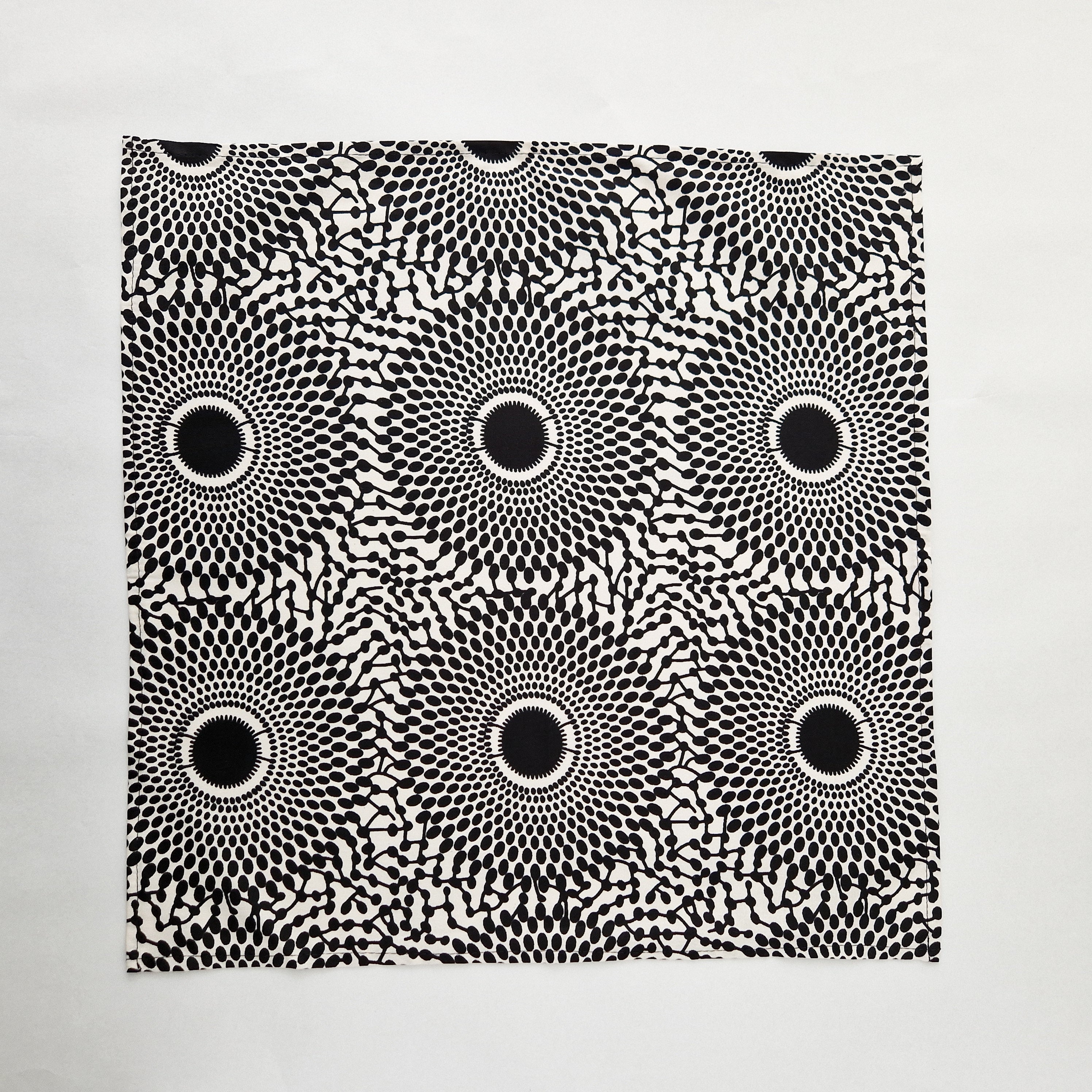 Black and off-white square fabric with a repeating pattern of concentric circles composed of small black ovals and thin