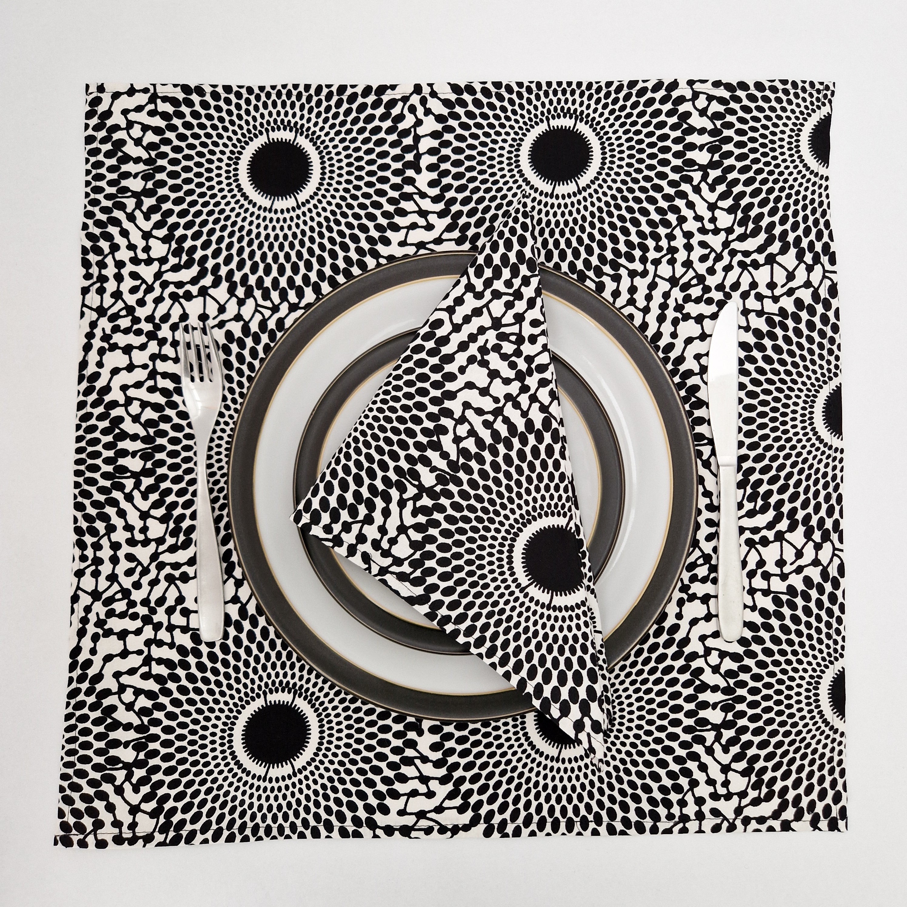 Black and white placemat with a radiating dot pattern, shown with plates, fork, and knife.