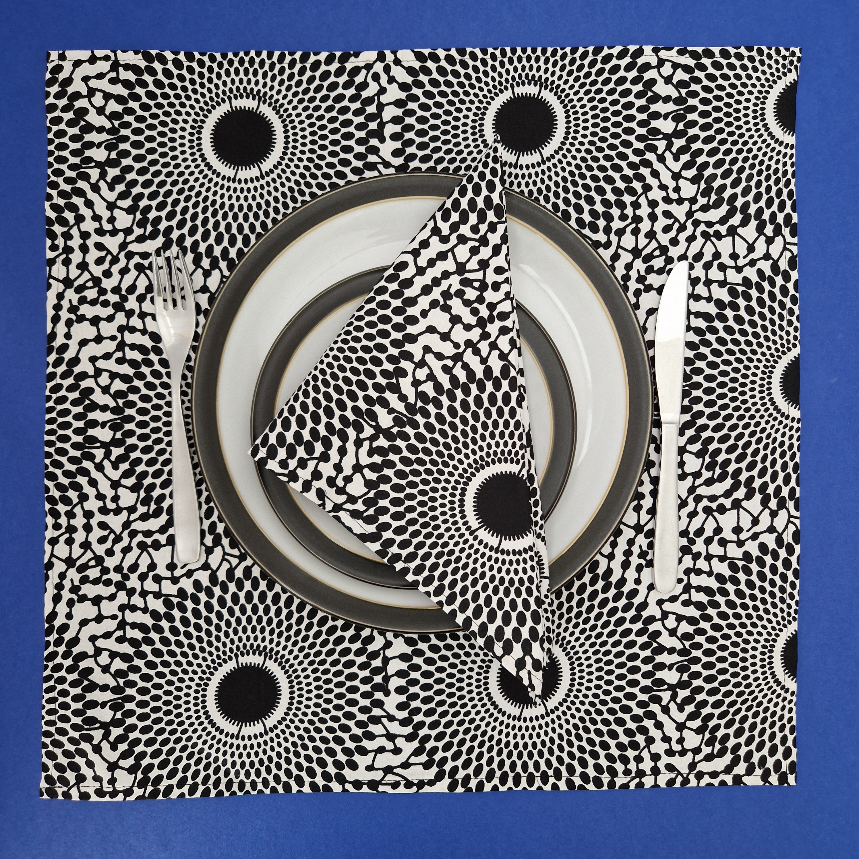 Black and white patterned placemat with concentric circles design, featuring folded napkin, plates, fork, and knife.