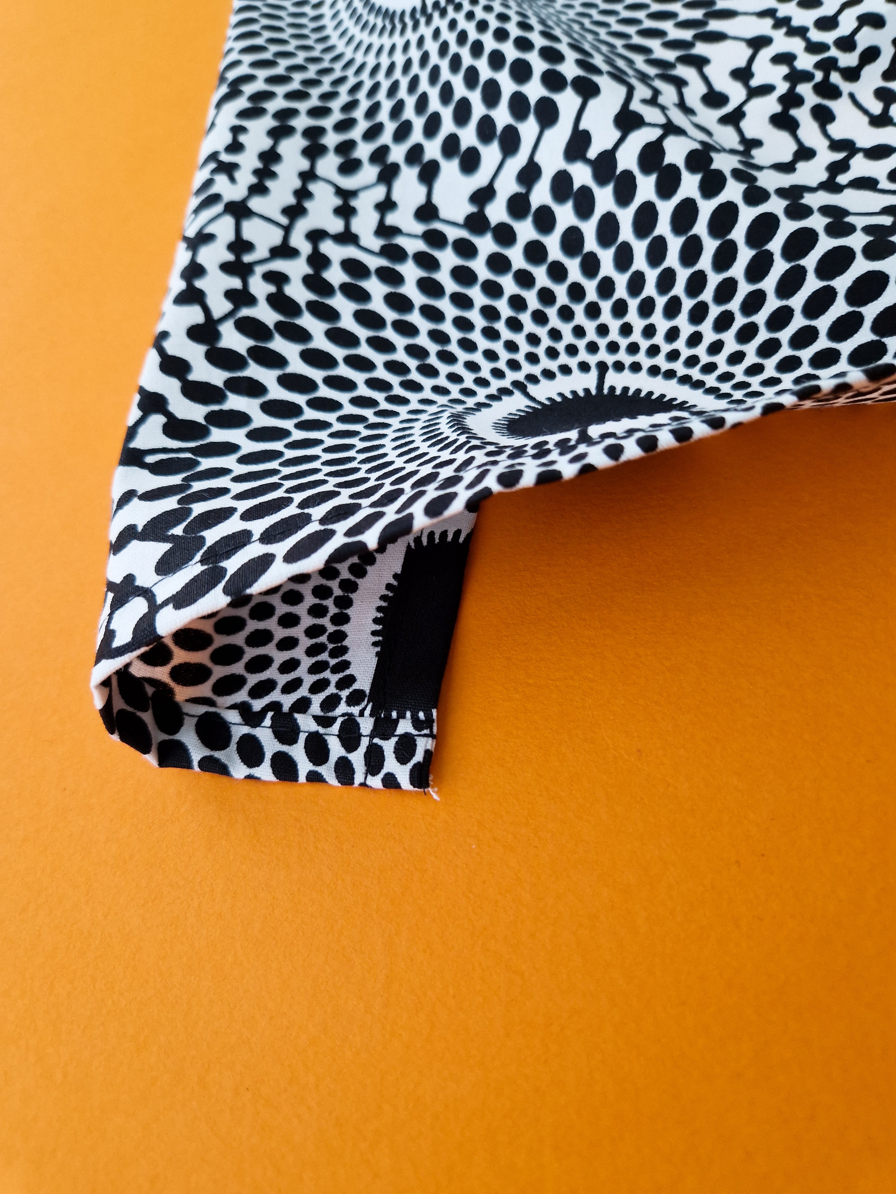 Close-up of fabric with a black and white concentric circle pattern.  The fabric is folded, showcasing a neatly finished hem.