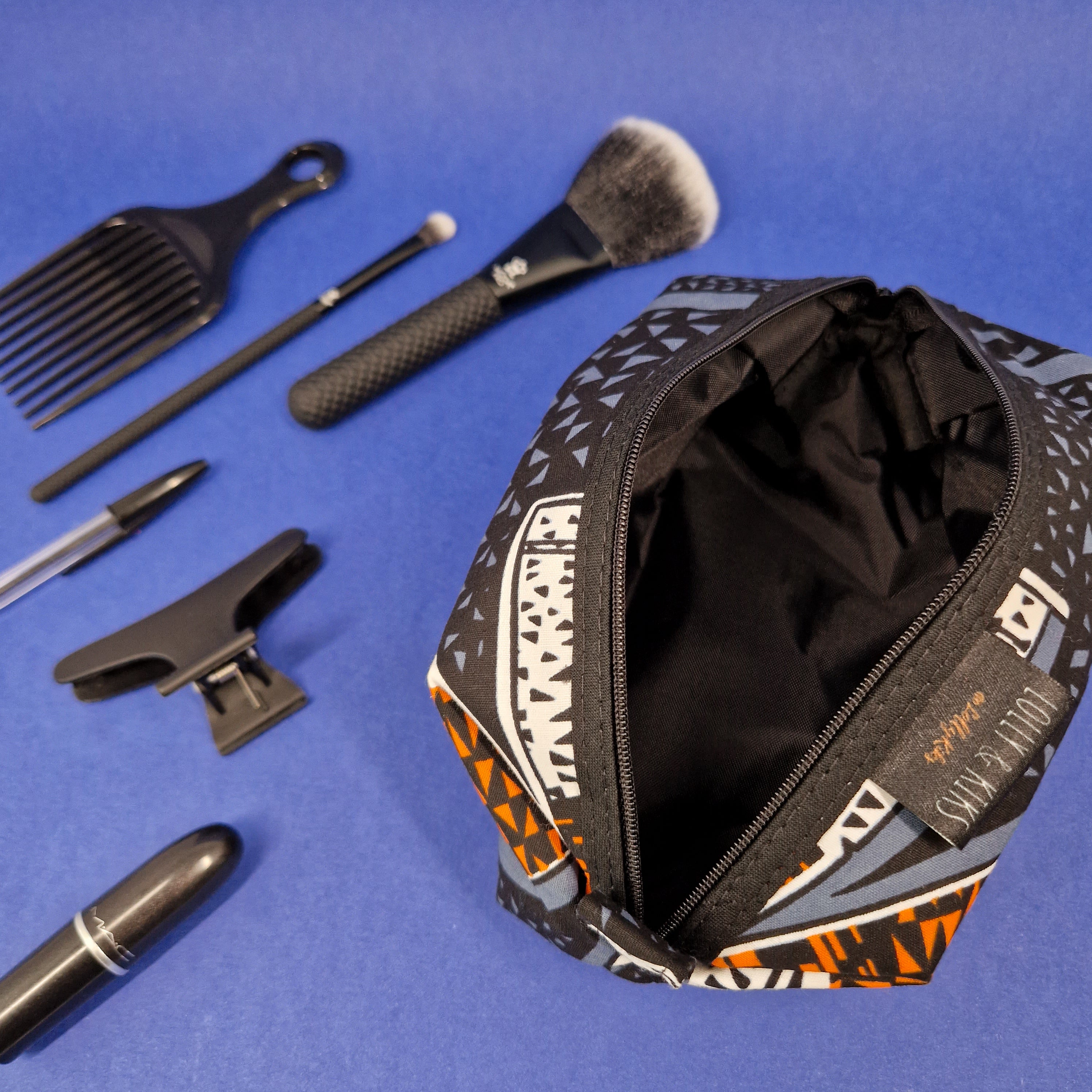 Open zippered cosmetic bag with geometric print in black, orange, and gray.