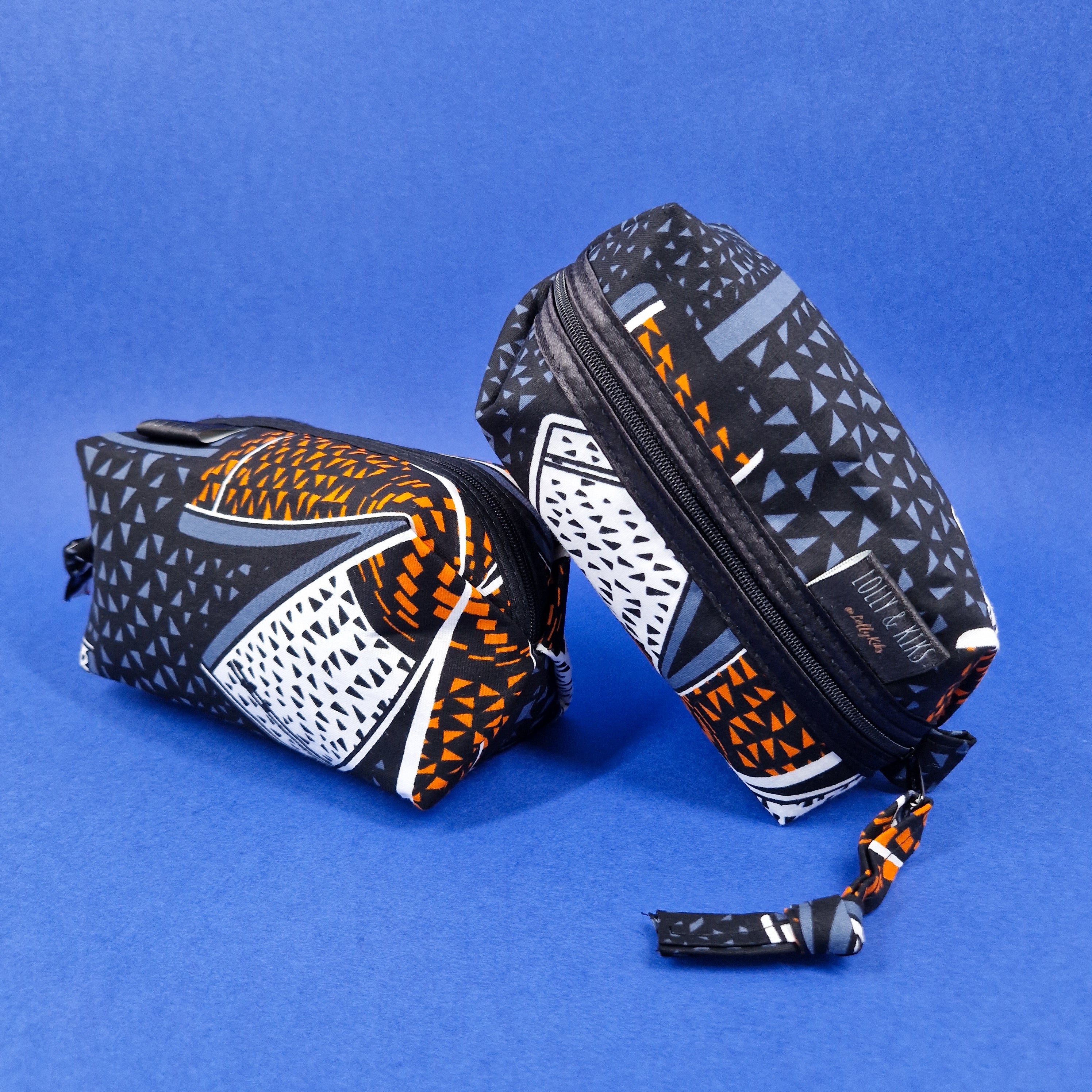 Two zippered rectangular cosmetic bags with a geometric black, orange, white, and gray print.