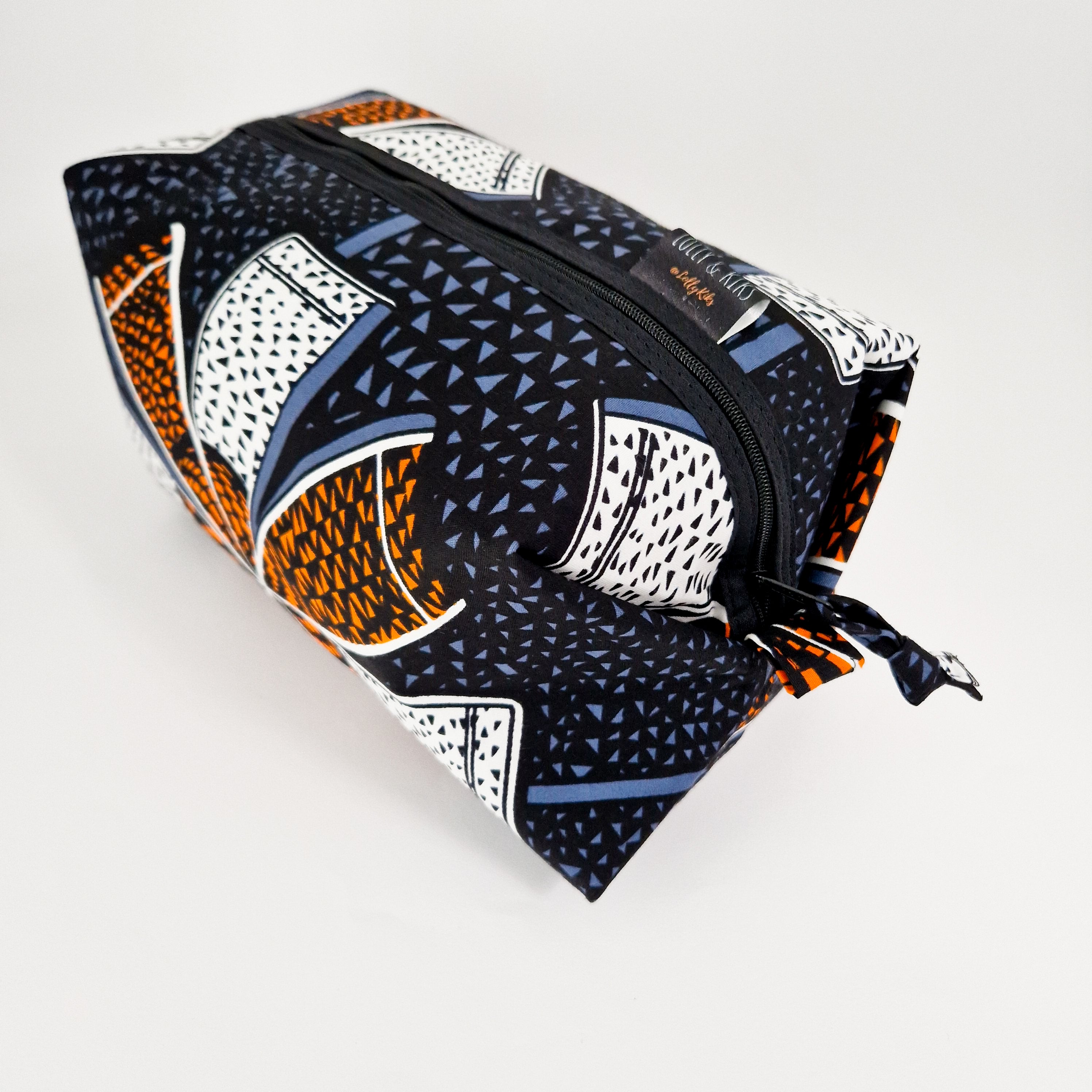 Rectangular zippered travel pouch with a black, orange, white, and blue geometric print.  The pouch has a fabric tie closure.