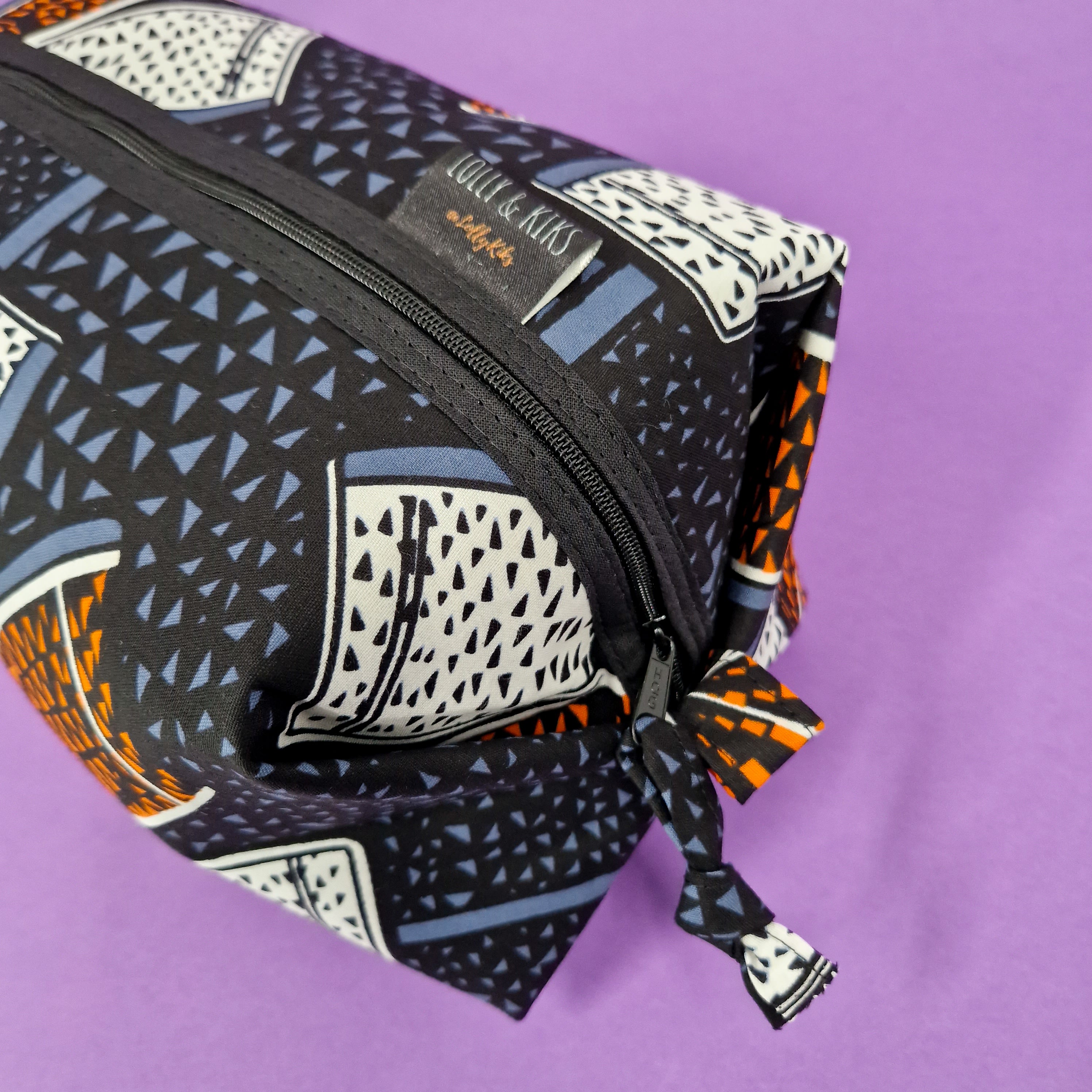 Rectangular zippered pouch with a black, white, orange, and blue geometric pattern.  The pouch has a fabric pull tab.