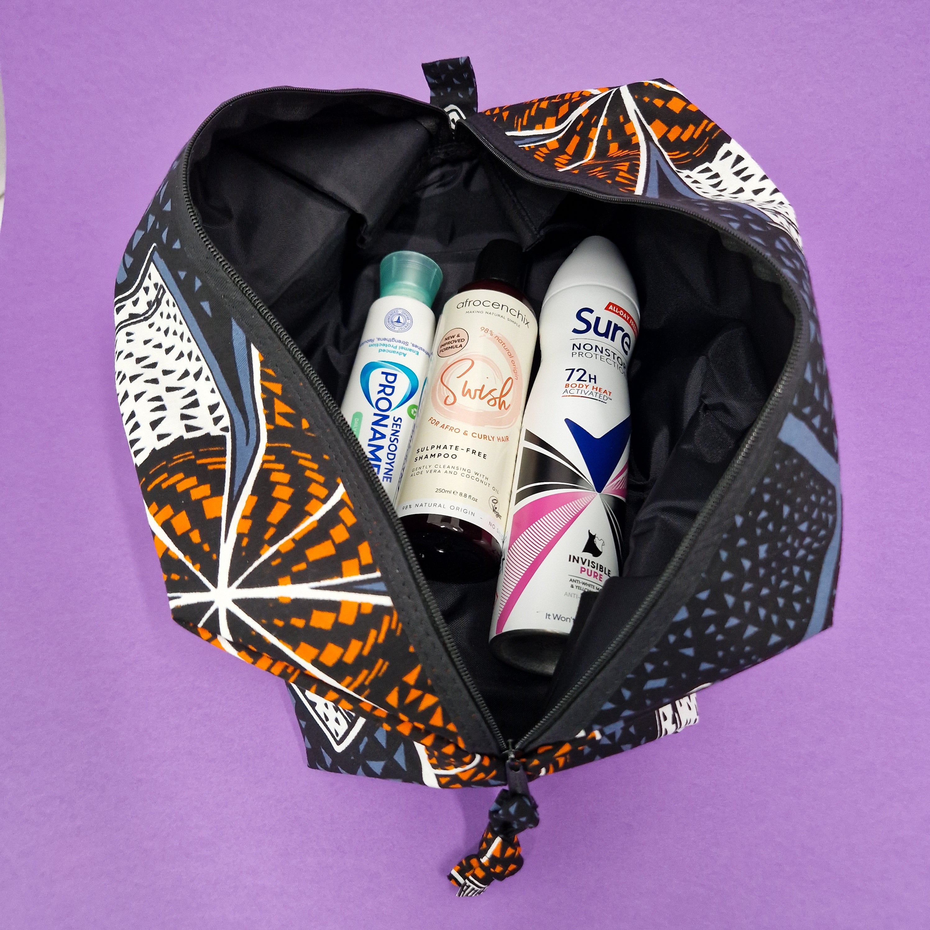 Black zippered travel bag with orange and blue geometric print, containing shampoo, conditioner, and deodorant.