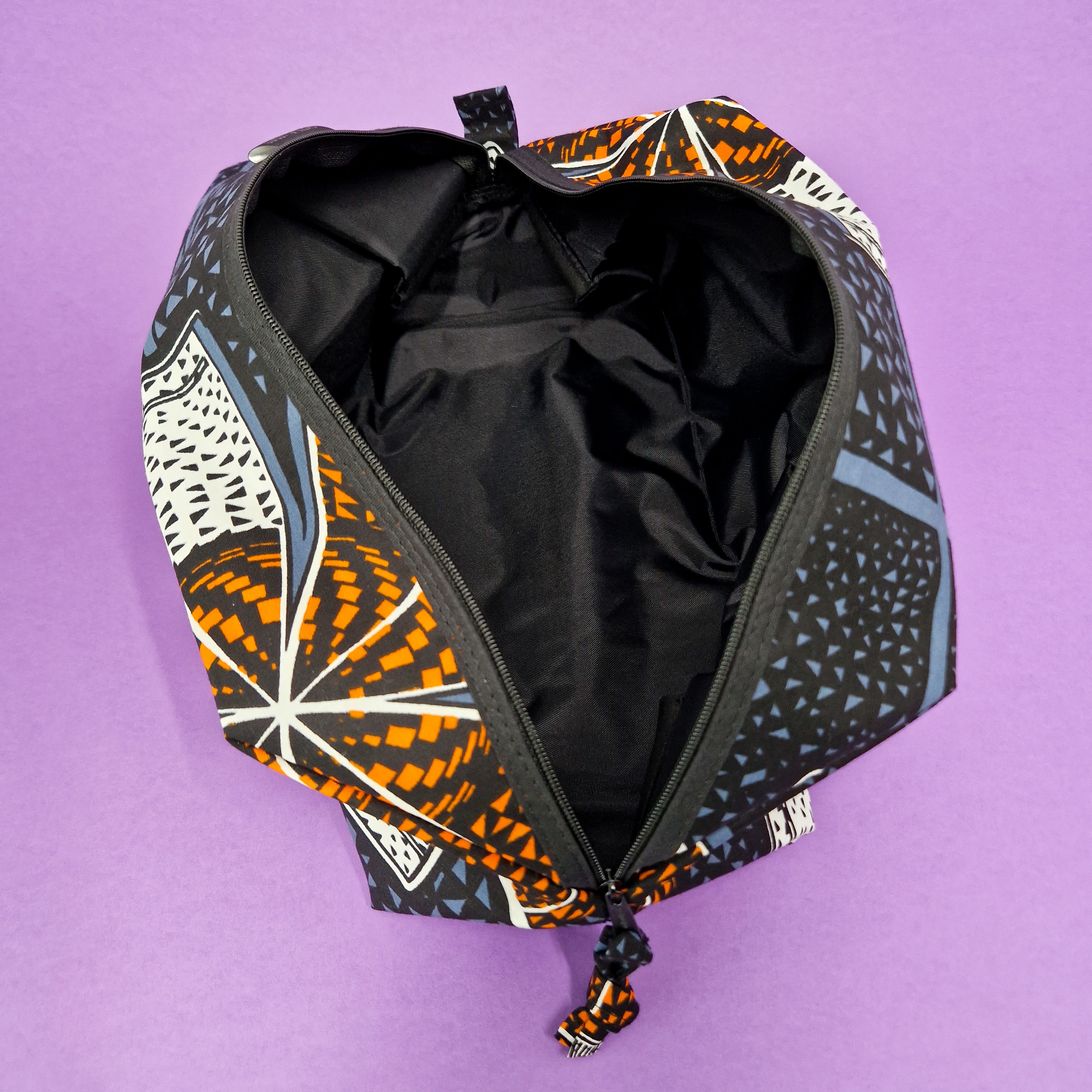 Open zippered travel bag with black interior and an orange, white, and blue geometric pattern.