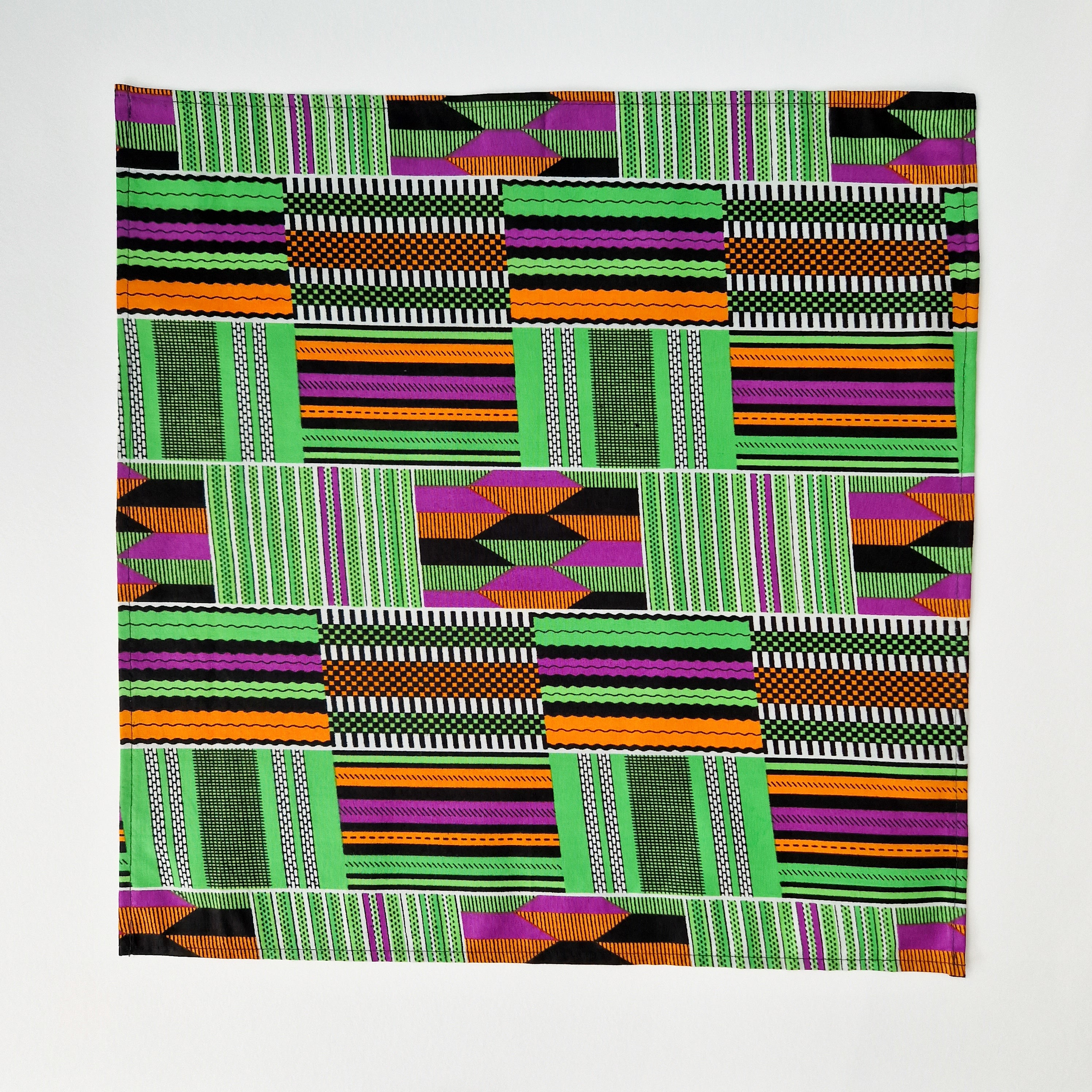 Square textile with a geometric pattern in green, orange, purple, black, and white.
