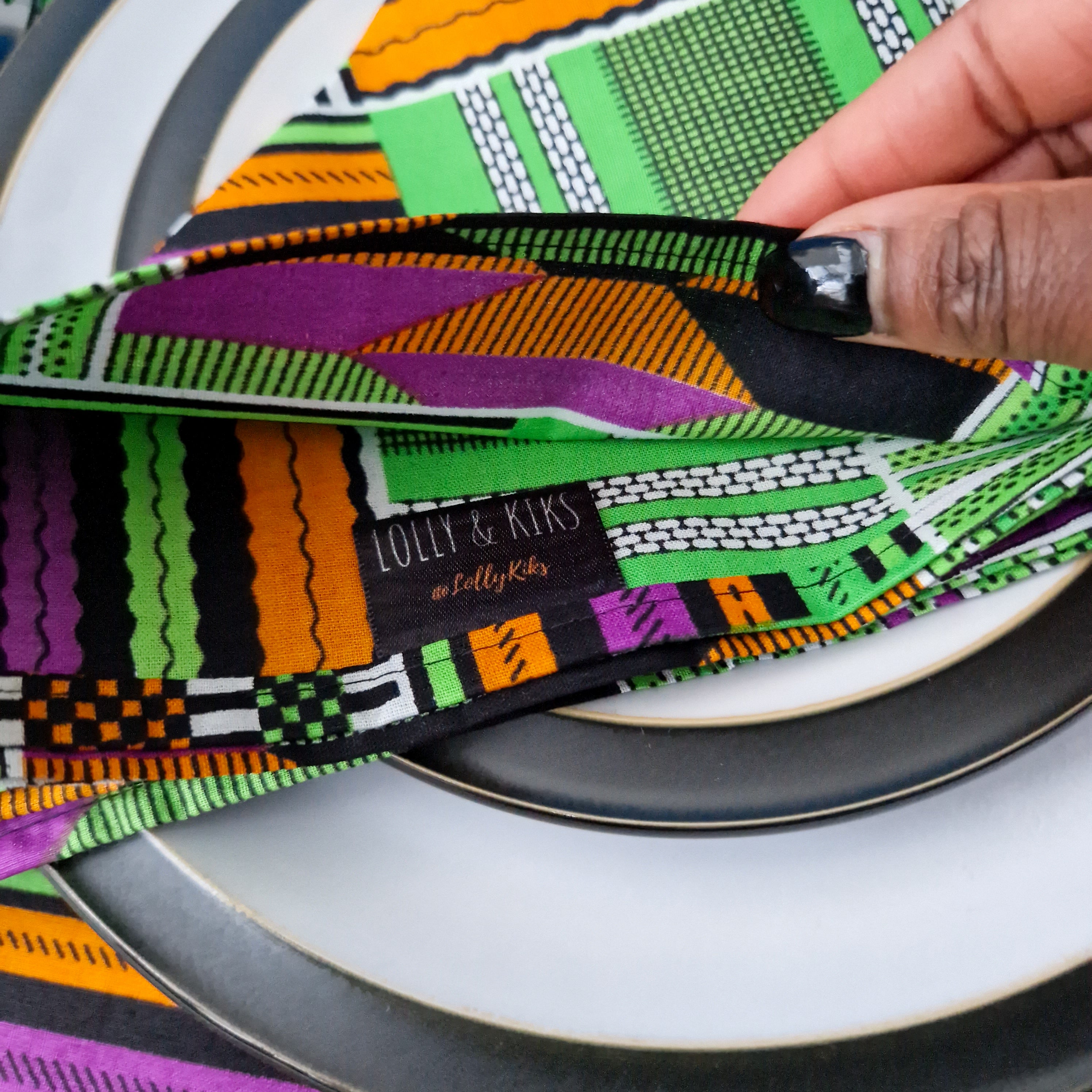 A folded fabric napkin with a vibrant geometric pattern in green, orange, purple, and black.