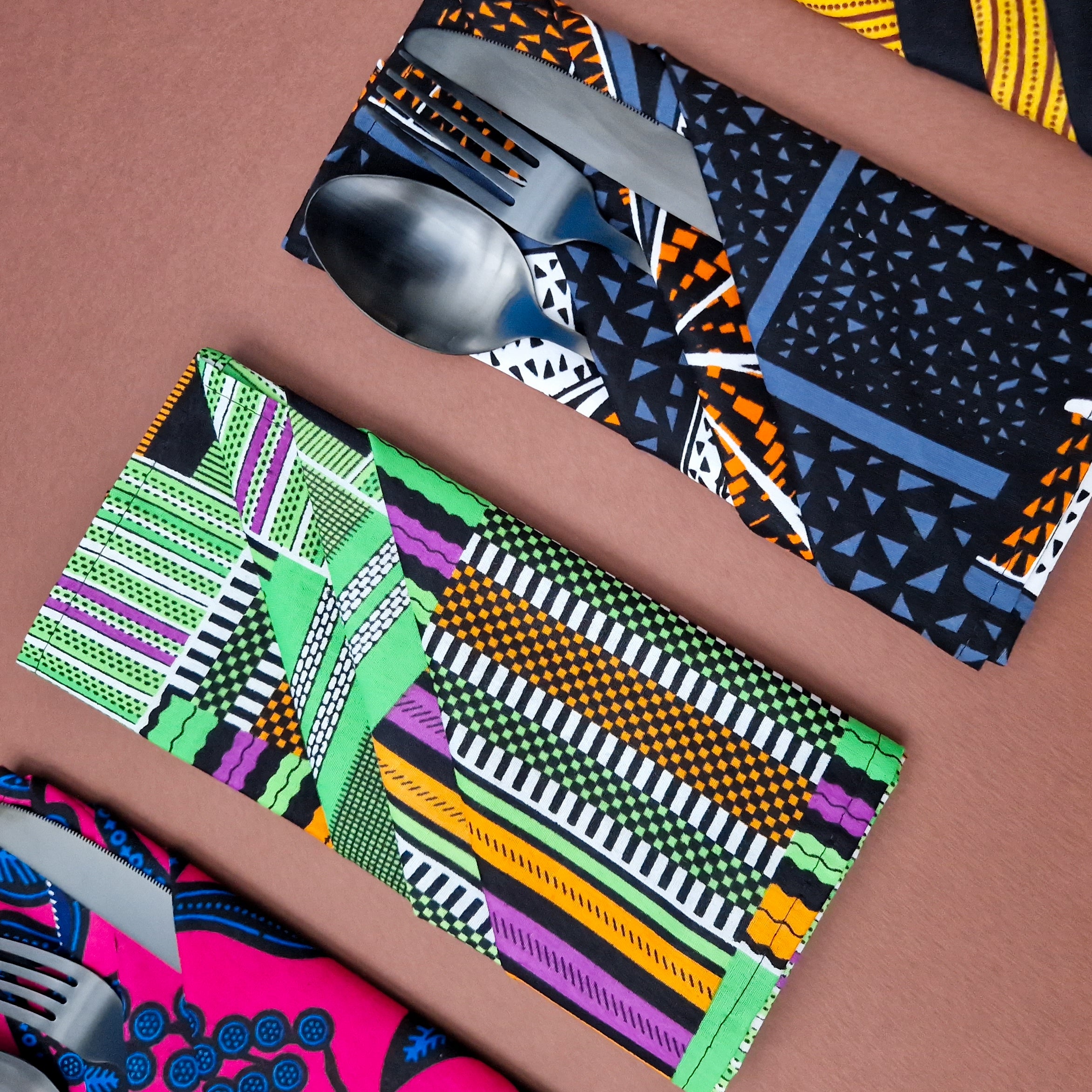 Flatware wrapped in vibrant, geometric patterned fabric napkins.  The napkins feature bold colors and designs.