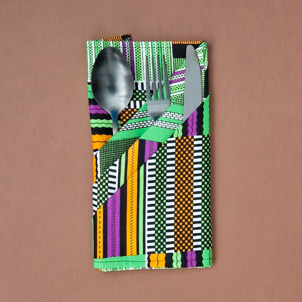 Spoon, fork, and knife tucked into a vibrant green, orange, purple, and black patterned napkin.