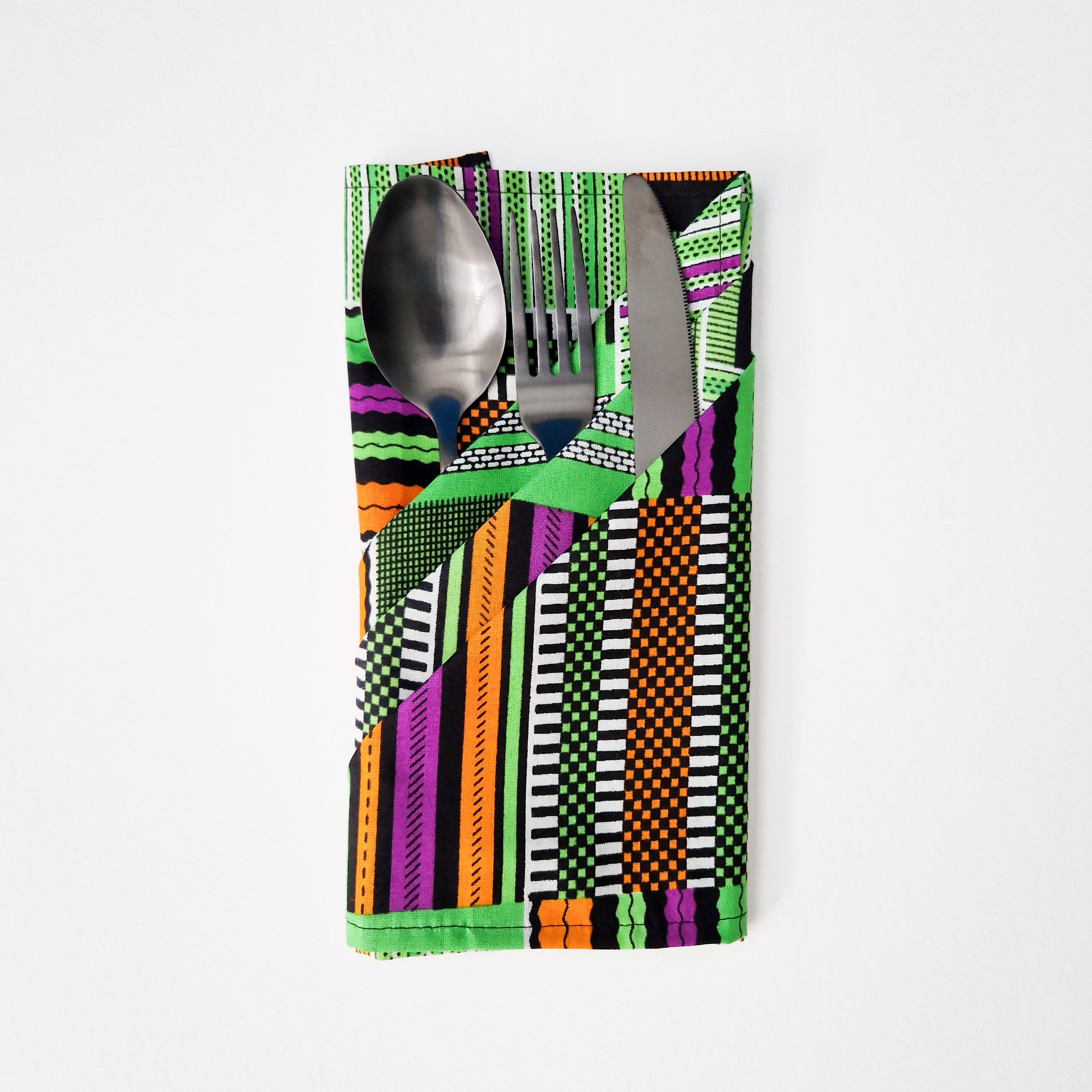 Silver spoon, fork, and knife neatly arranged within a folded napkin featuring a vibrant green, orange, purple, and black