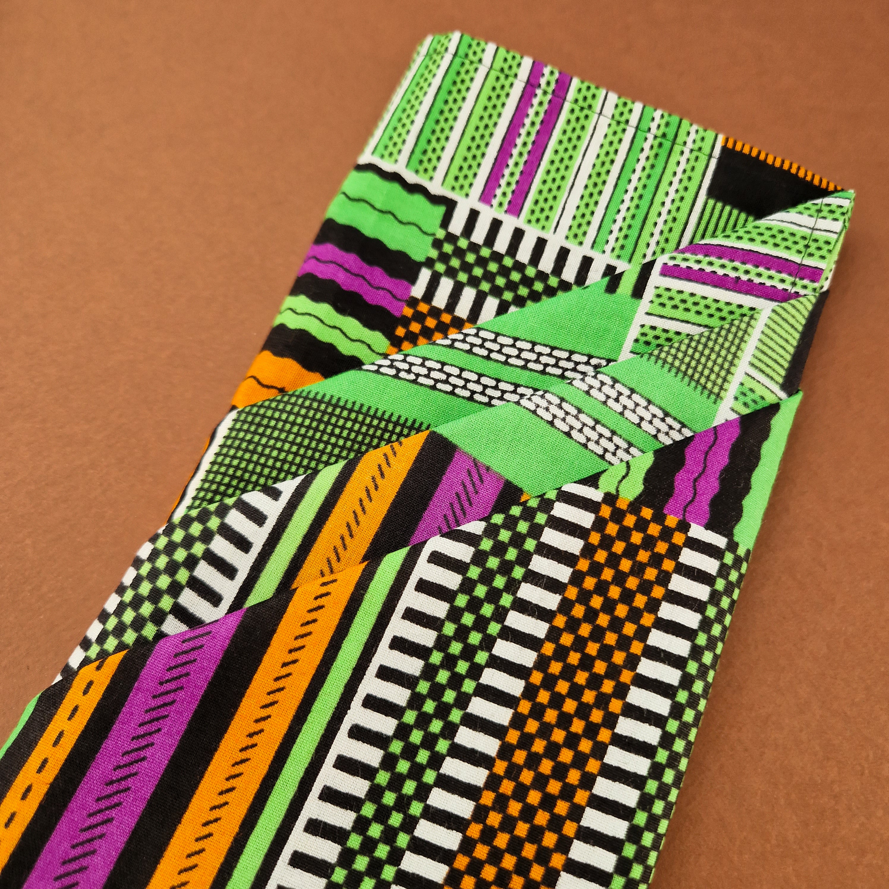 Folded fabric with a vibrant geometric pattern in green, orange, purple, black, and white.