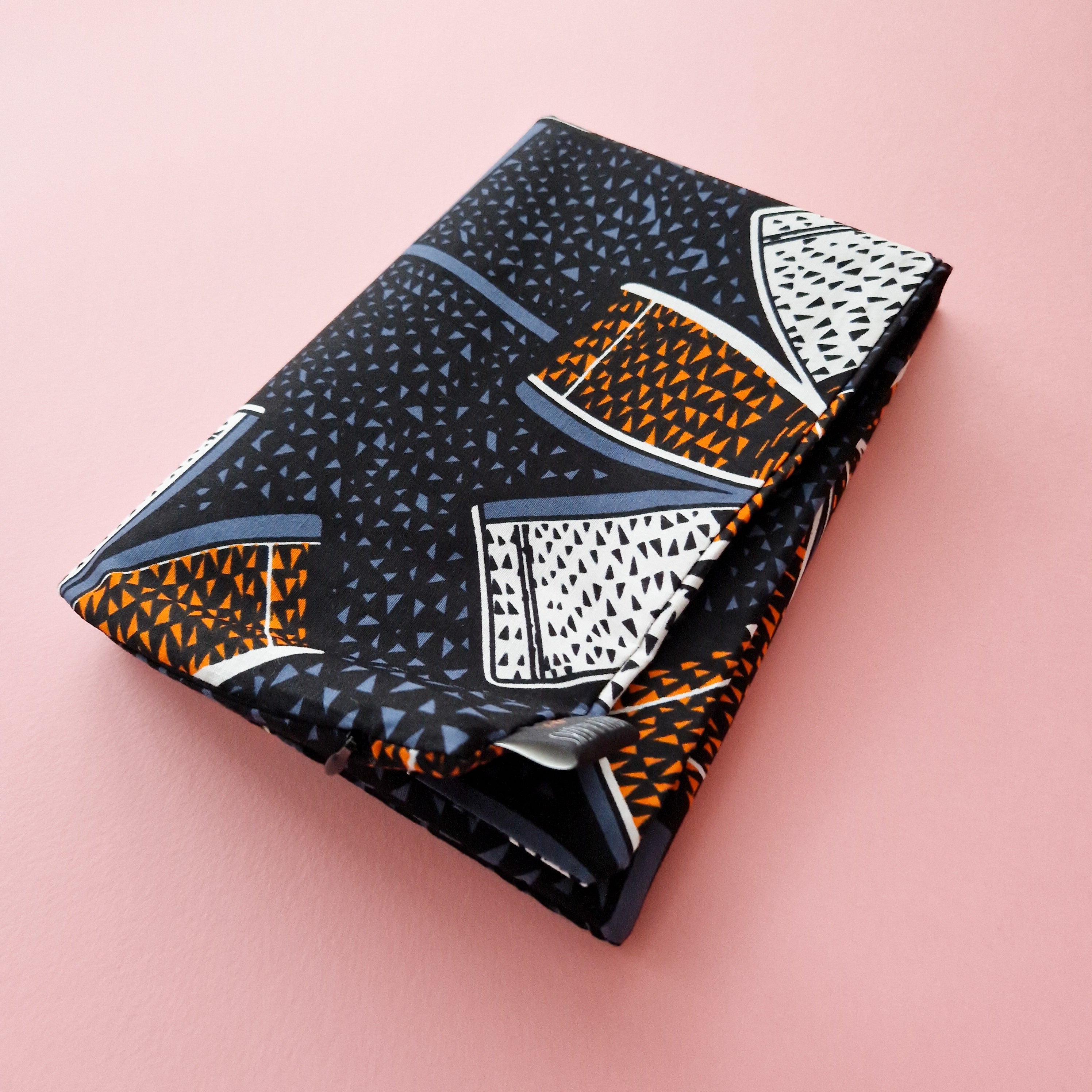 Small folded pouch with a dark fabric featuring a geometric pattern in orange, white, and blue.