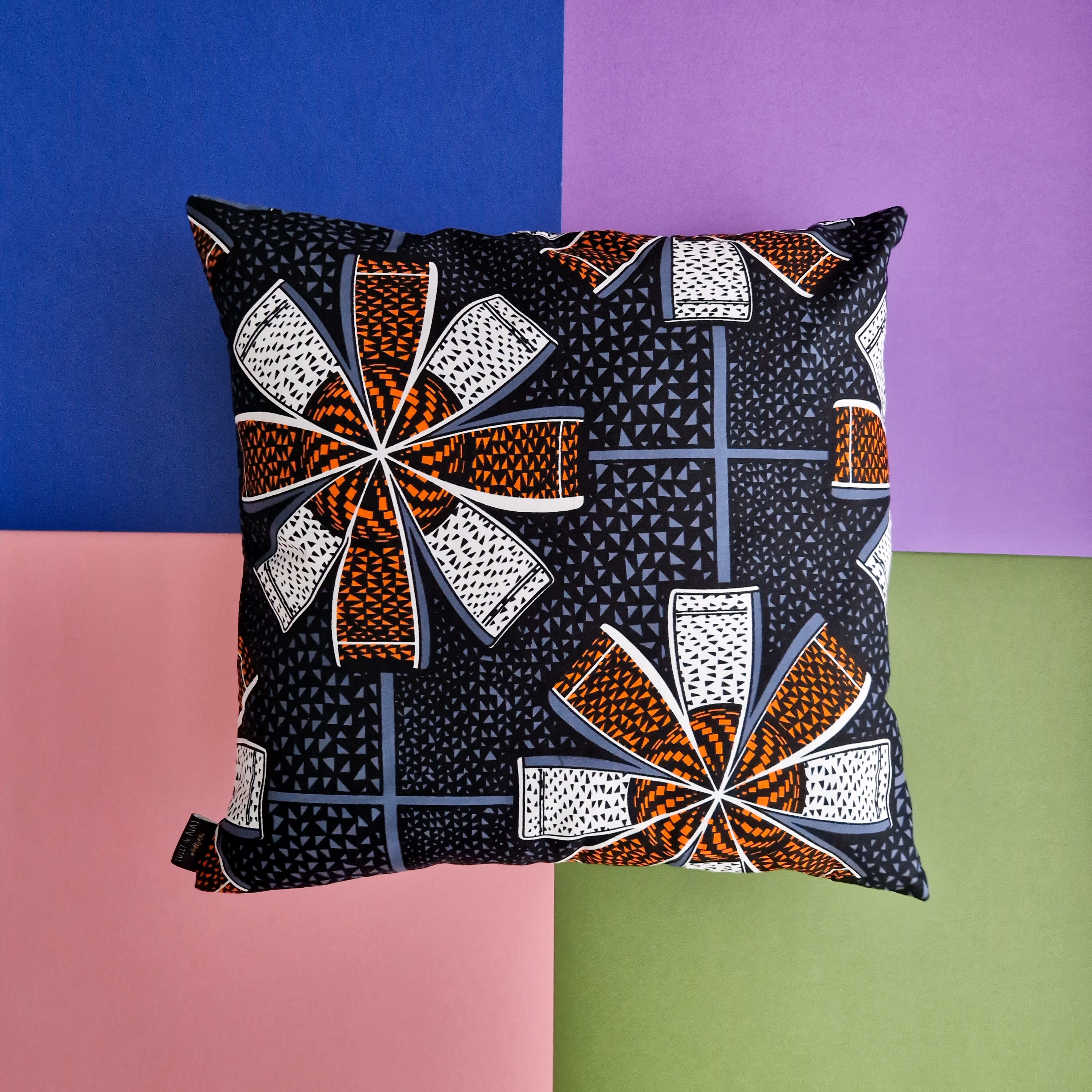 Square cushion with a dark background and a repeating pattern of orange, white, and gray stylized flower shapes.