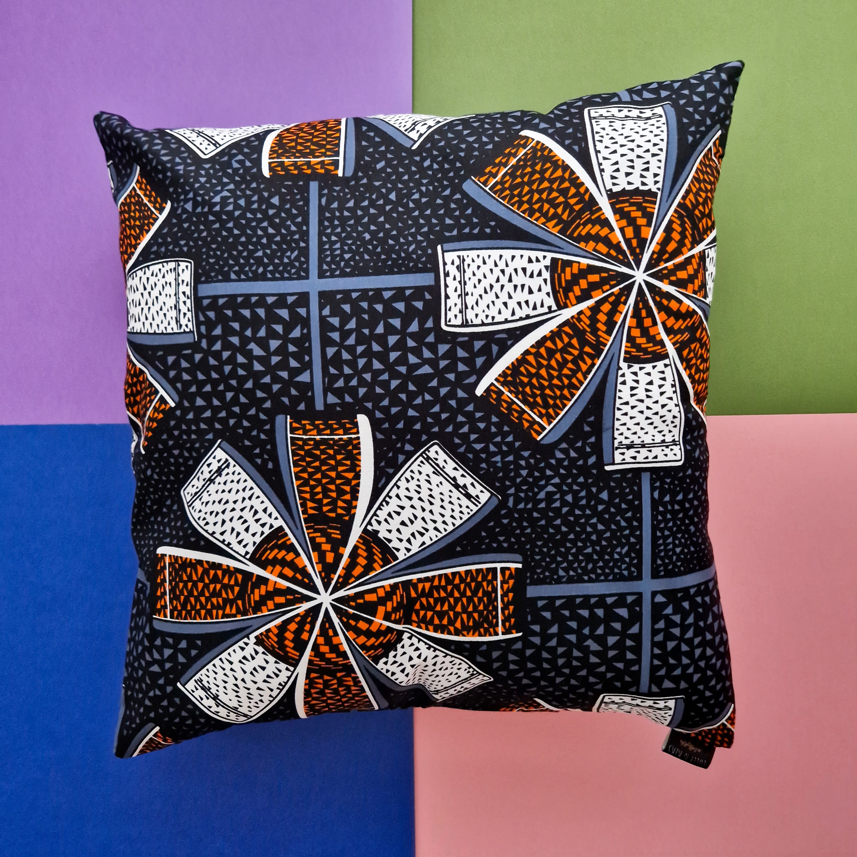 Square cushion with a dark background featuring a repeating pattern of orange, white, and gray geometric shapes resembling