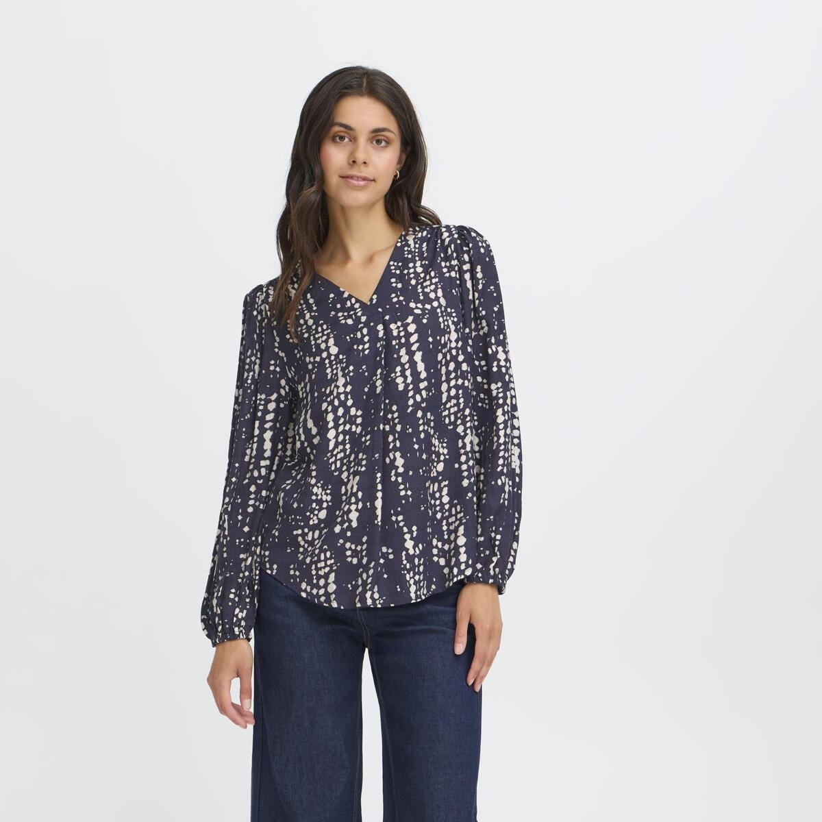Woman wearing a patterned blouse and jeans on a white background