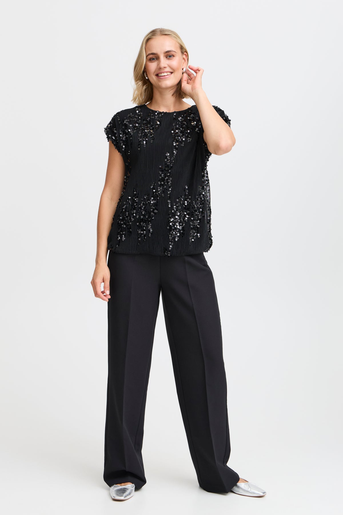 Black sequined pleated top with short sleeves, paired with wide-leg black trousers.