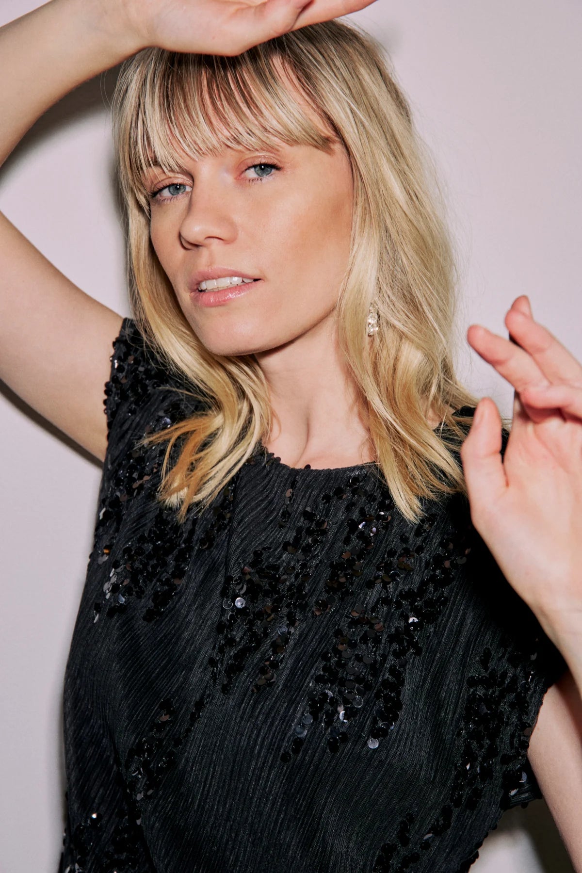 Black sequined short-sleeved top with pleated fabric. The sequins are dark and scattered across the garment.