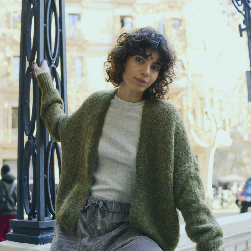 Woman wearing a green cardigan over a white sweater, standing in front of a decorative metal gate.
