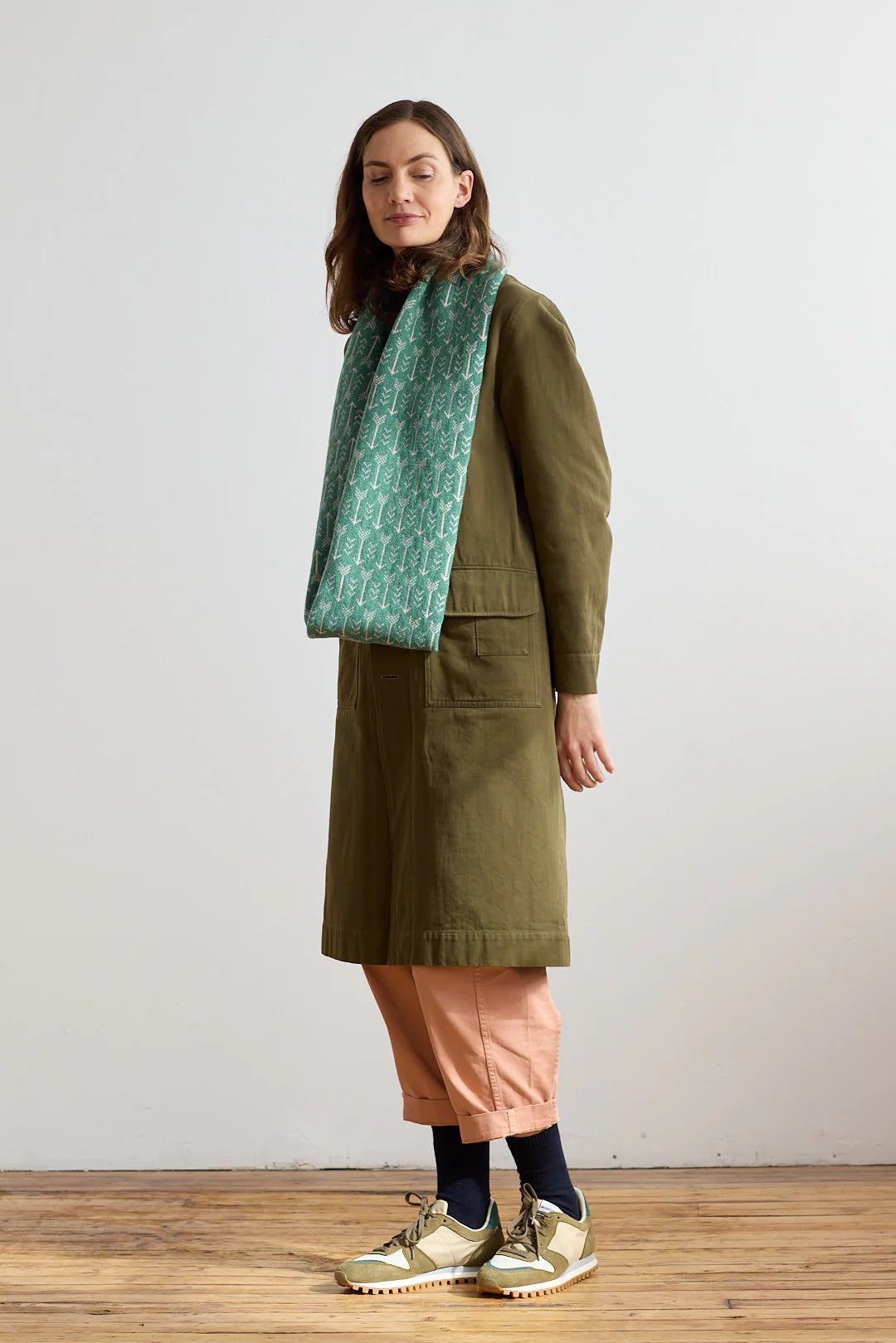 Green patterned wool scarf draped around a model wearing an olive green coat and light pink cropped pants.