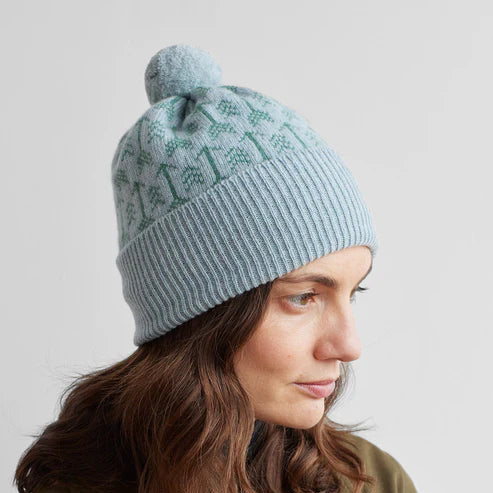 Light blue knit beanie with a pompom and a repeating green tree pattern.