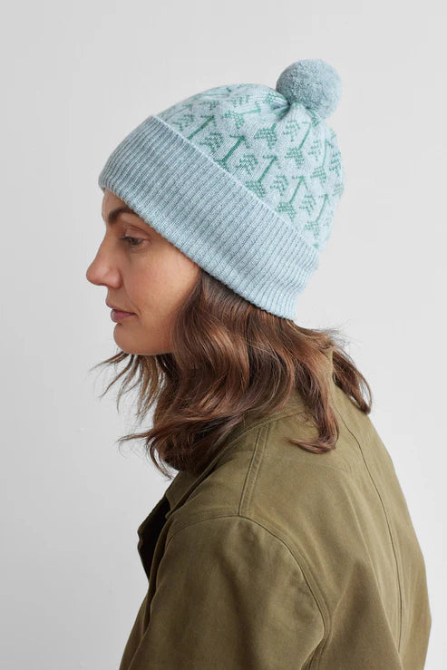 Light blue knit beanie with a pompom and green tree pattern.