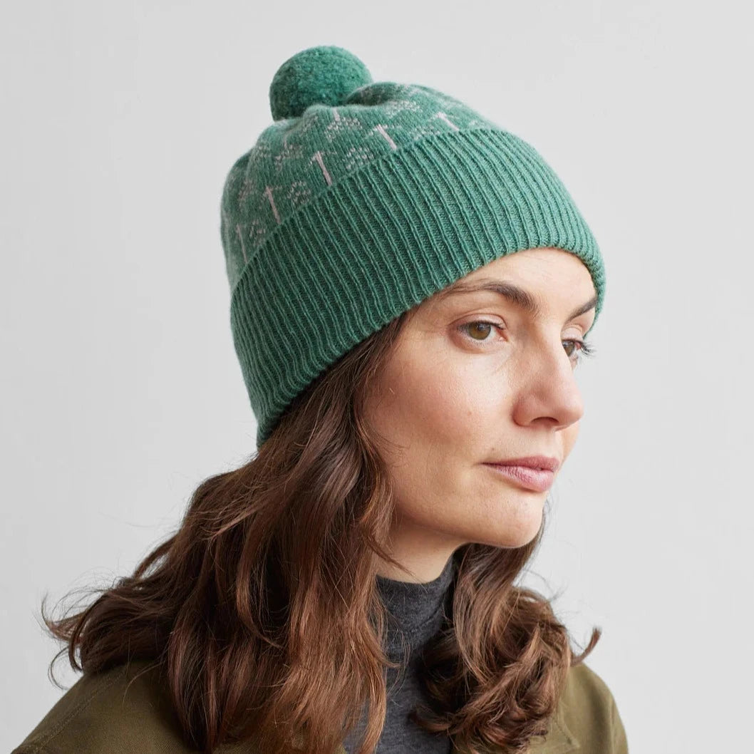 Green wool beanie with a pompom and subtle patterned detail.