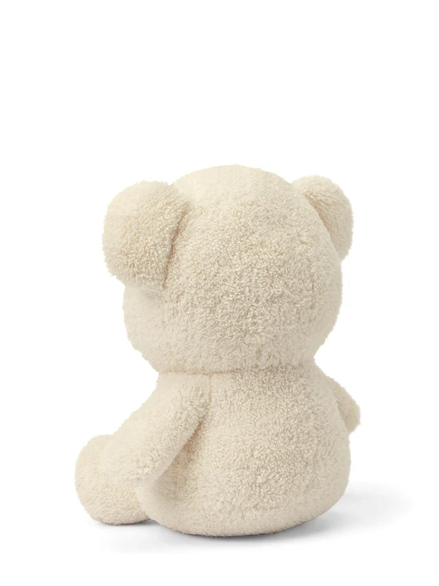 Cream-colored plush teddy bear sitting down, viewed from behind. The bear has a fluffy, textured coat.