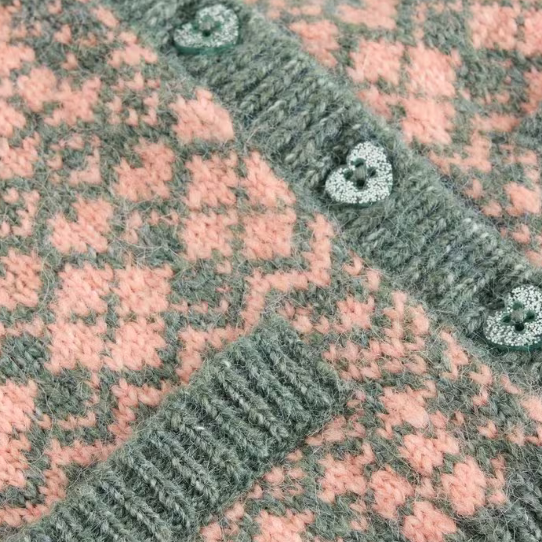 Close-up of a grey and pink knitted cardigan with heart-shaped buttons. The fabric features a textured pattern.