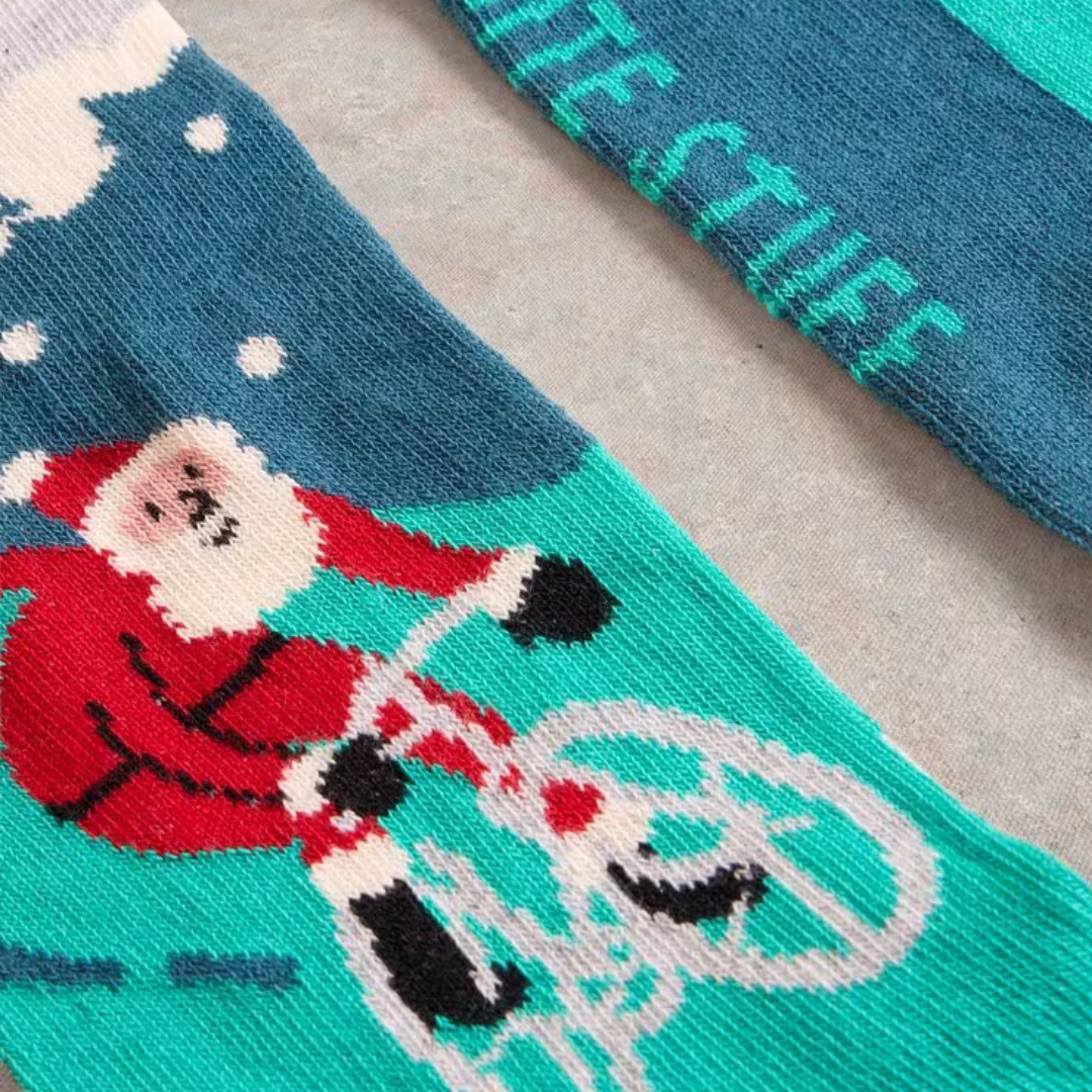 Christmas socks featuring Santa Claus riding a bicycle on a teal background.