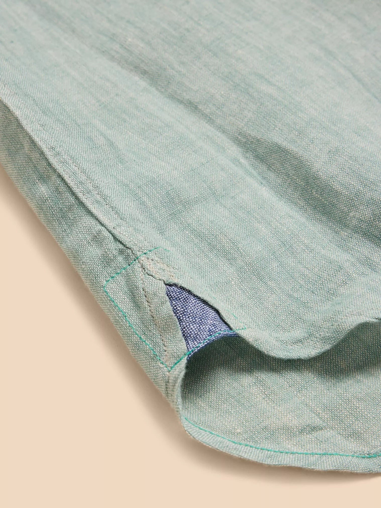 Close-up of a light teal linen shirt's hem, showcasing its textured fabric and teal and navy blue interior detail with green