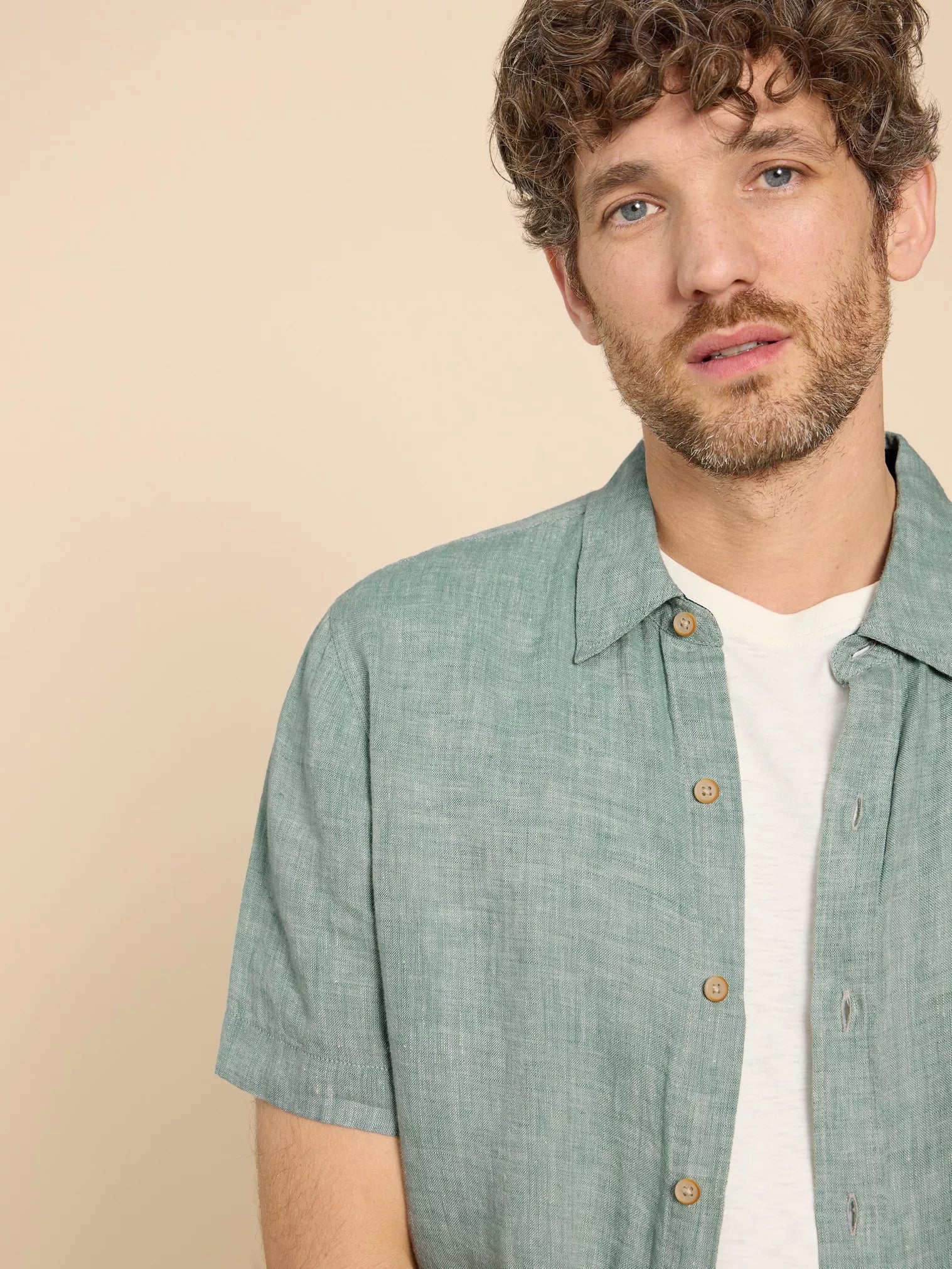 Sage green linen short-sleeve shirt with a textured weave and natural buttons.