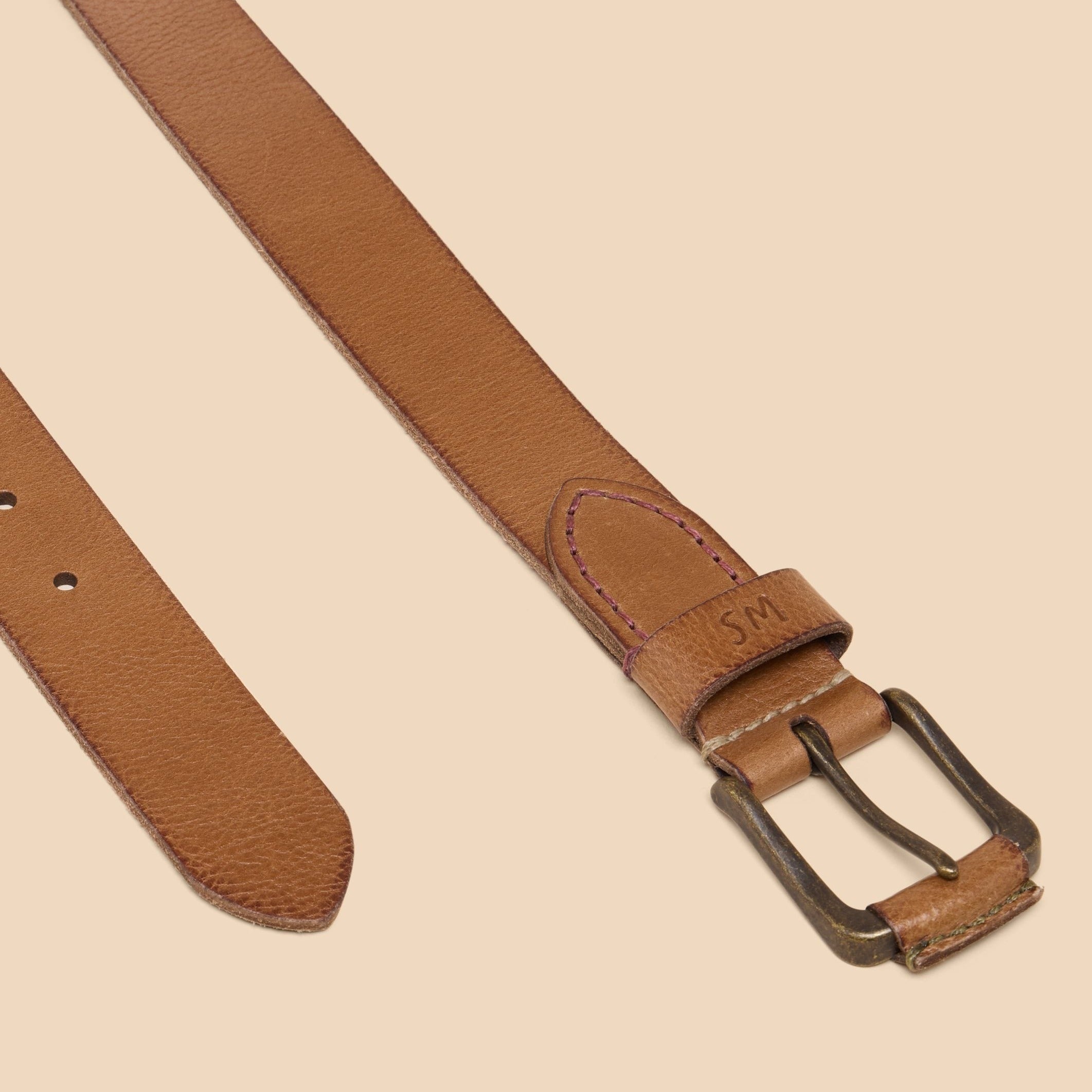 Brown leather belt with antique brass buckle and subtle stitching detail. The buckle is marked with "SM".