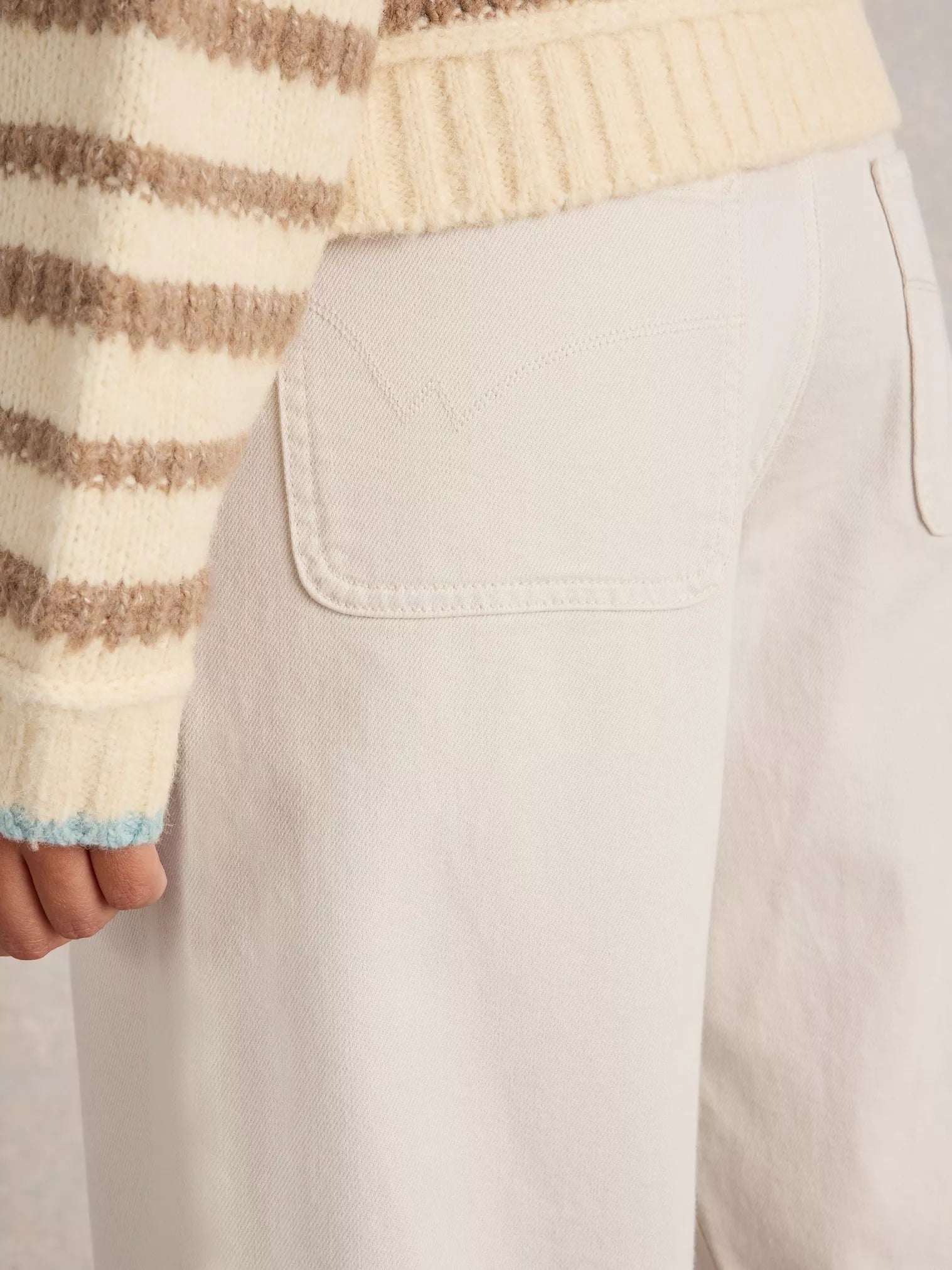 Off-white high-waisted pants with a back patch pocket, shown with a portion of a cream and brown striped sweater.