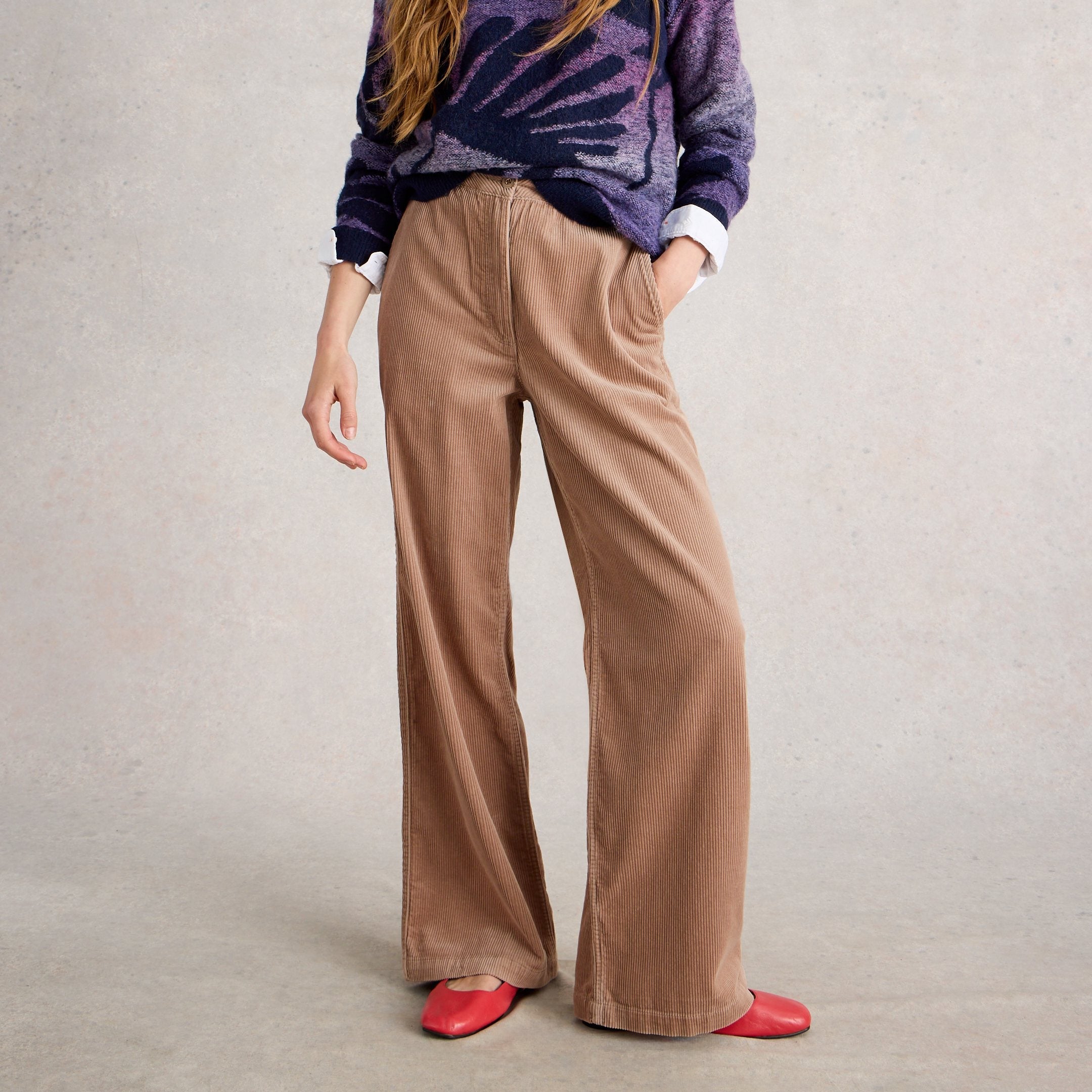 Woman wearing a purple tie-dye sweater and brown pants on a light gray background