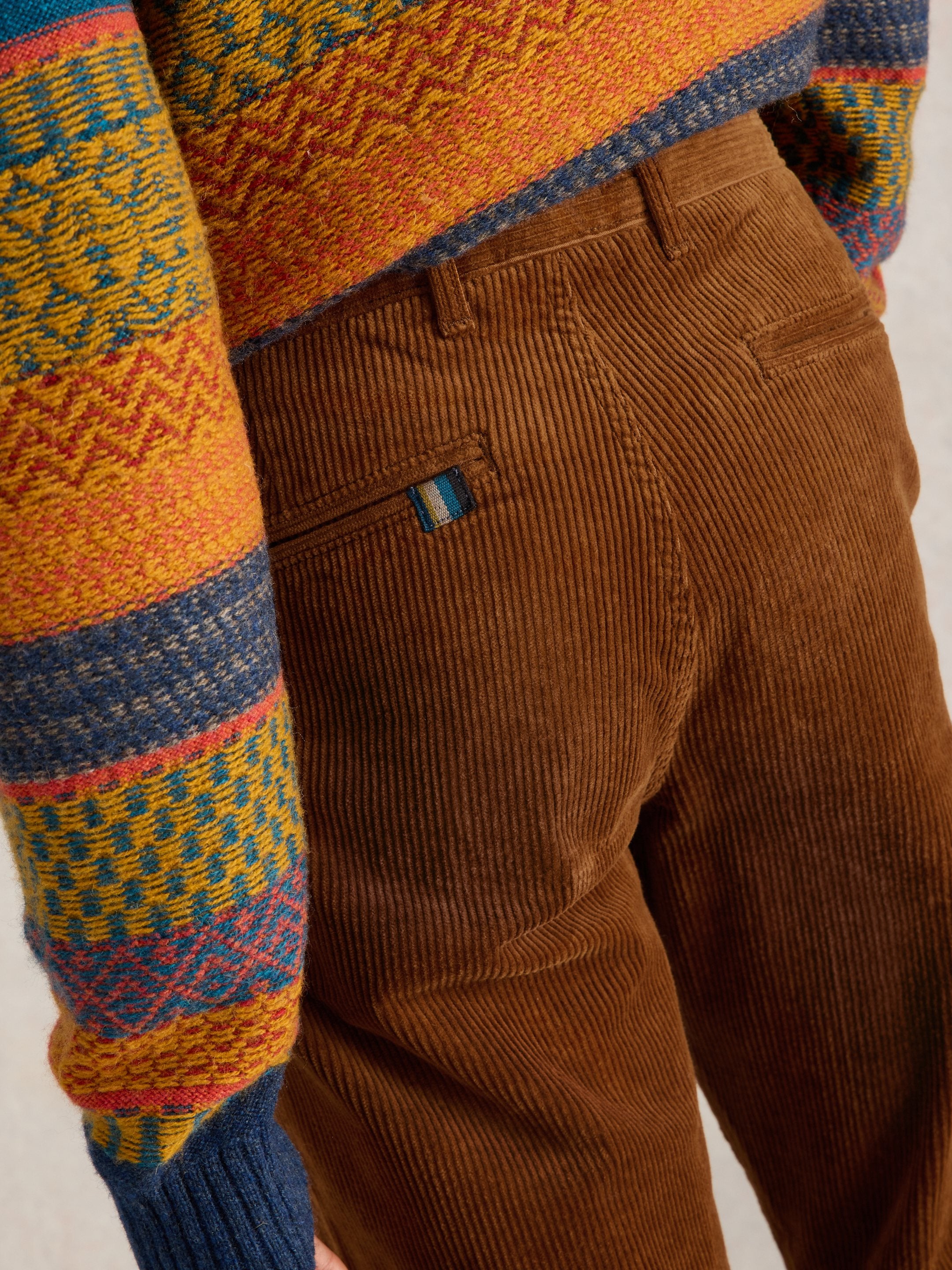 Close-up of brown corduroy pants with a colorful patterned sweater sleeve.
