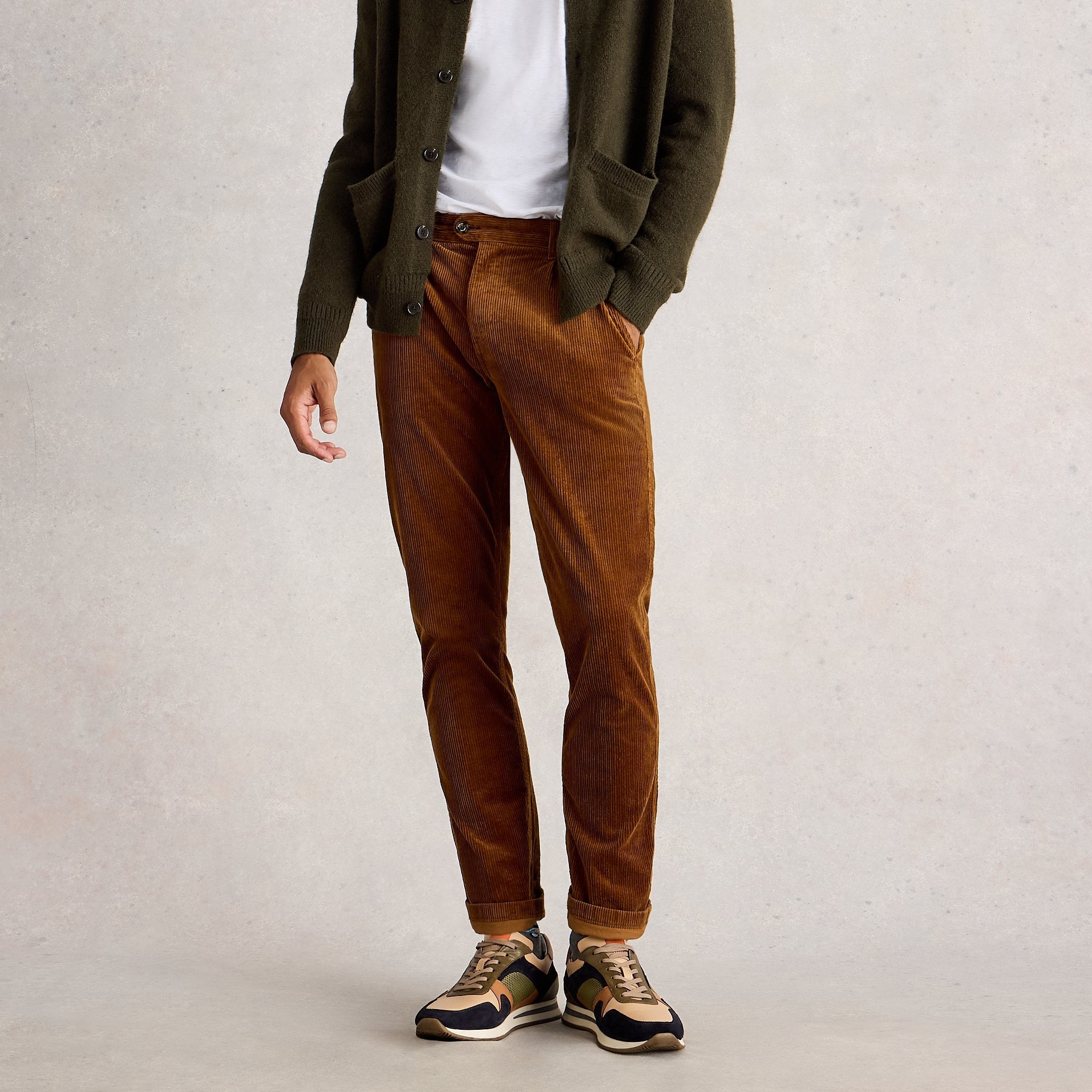 Man wearing a green cardigan, white shirt, brown pants, and sneakers on a plain background