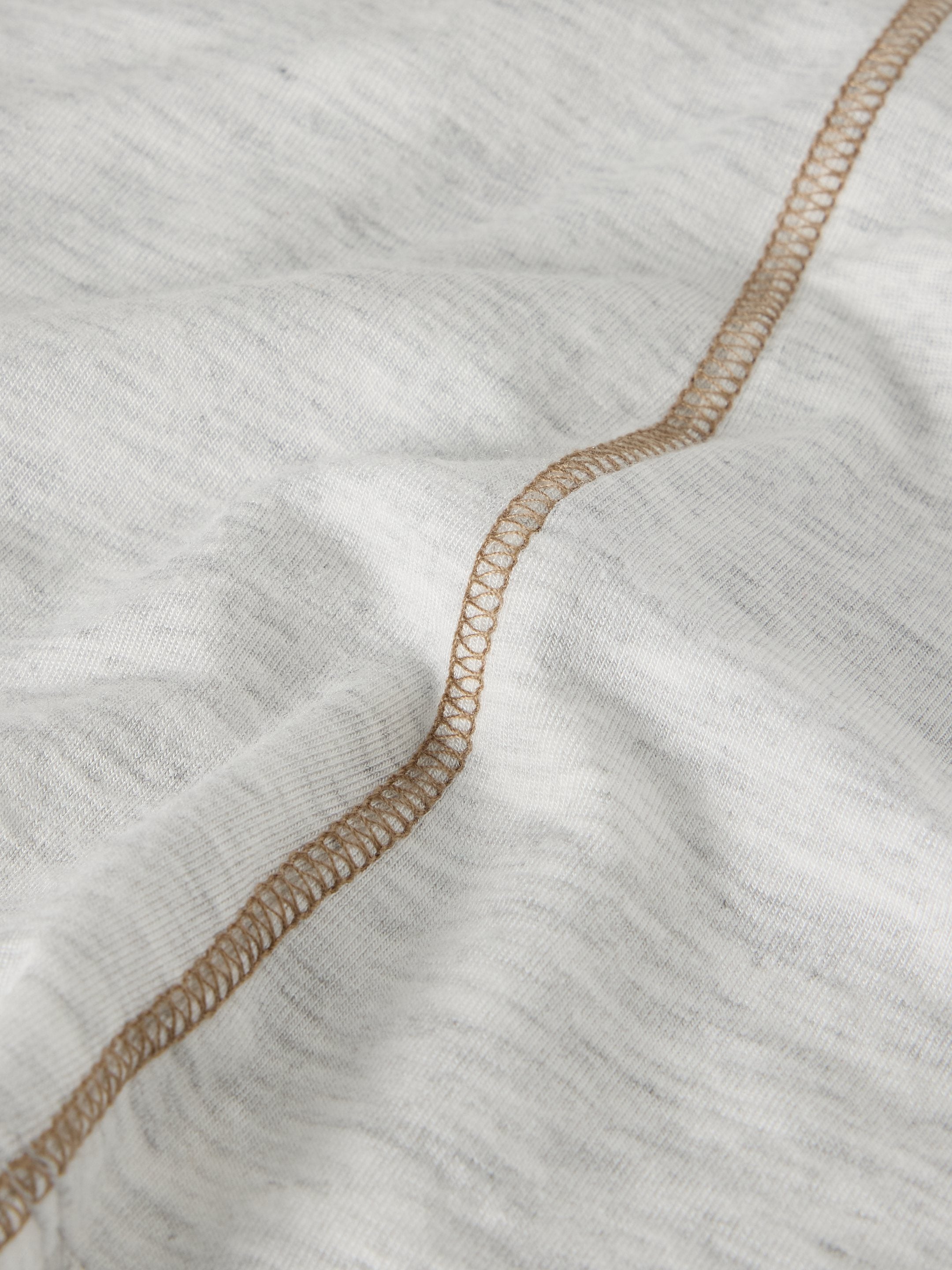 Close-up of light gray fabric with a tan topstitching detail.
