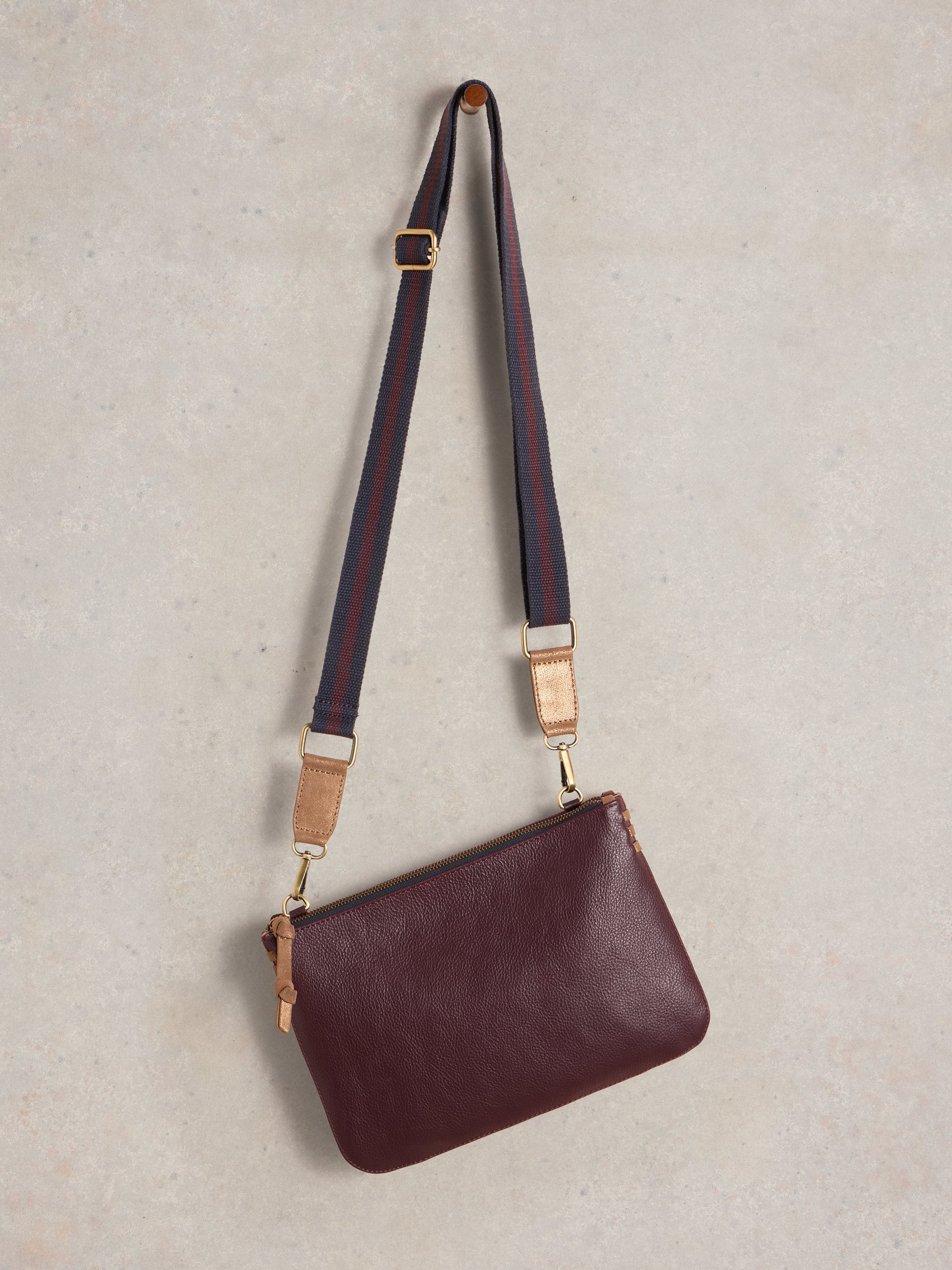 Burgundy leather crossbody bag with a dark navy and burgundy striped strap and gold-toned hardware.