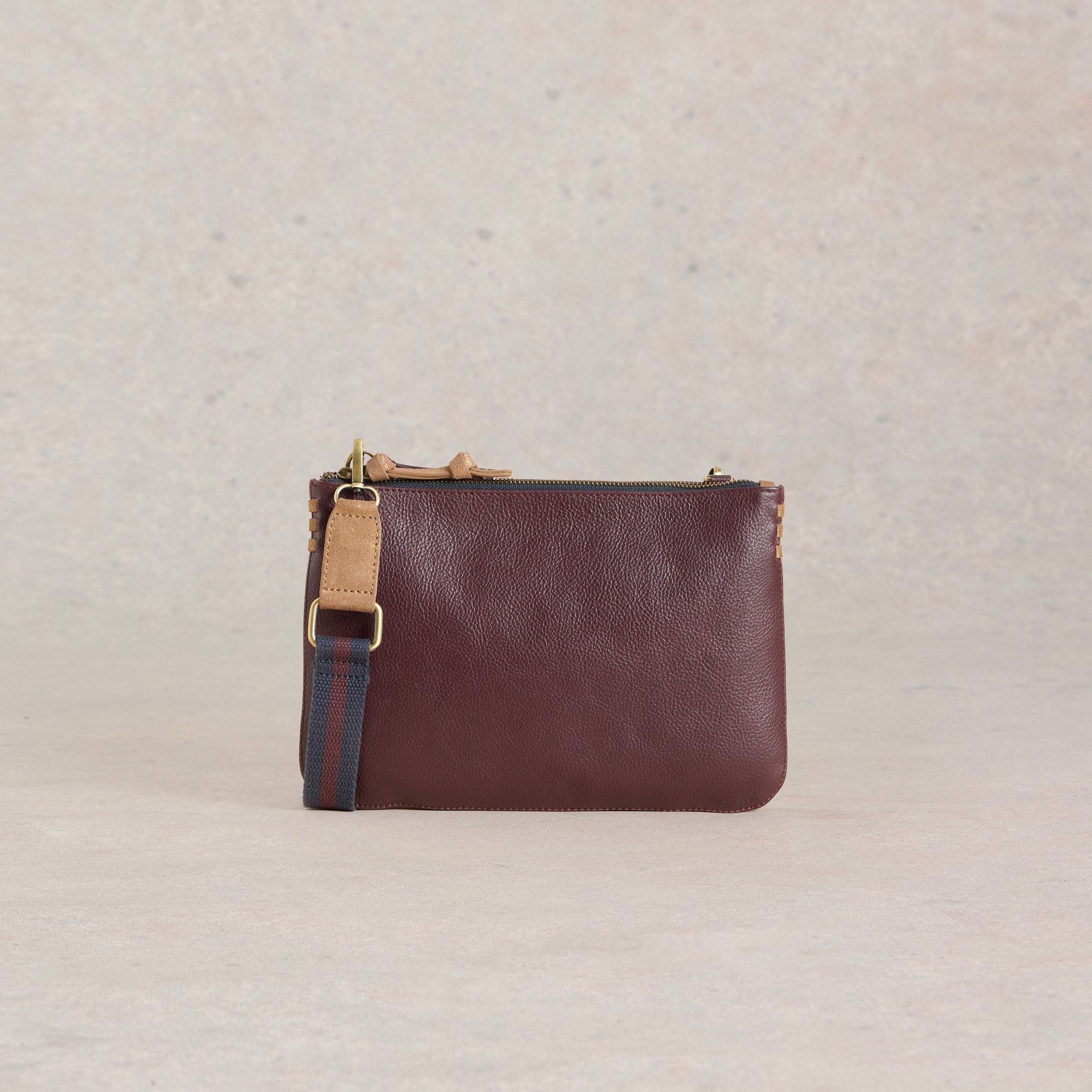 Burgundy leather crossbody bag with a zip closure, tan leather accents, and a navy and burgundy striped strap.